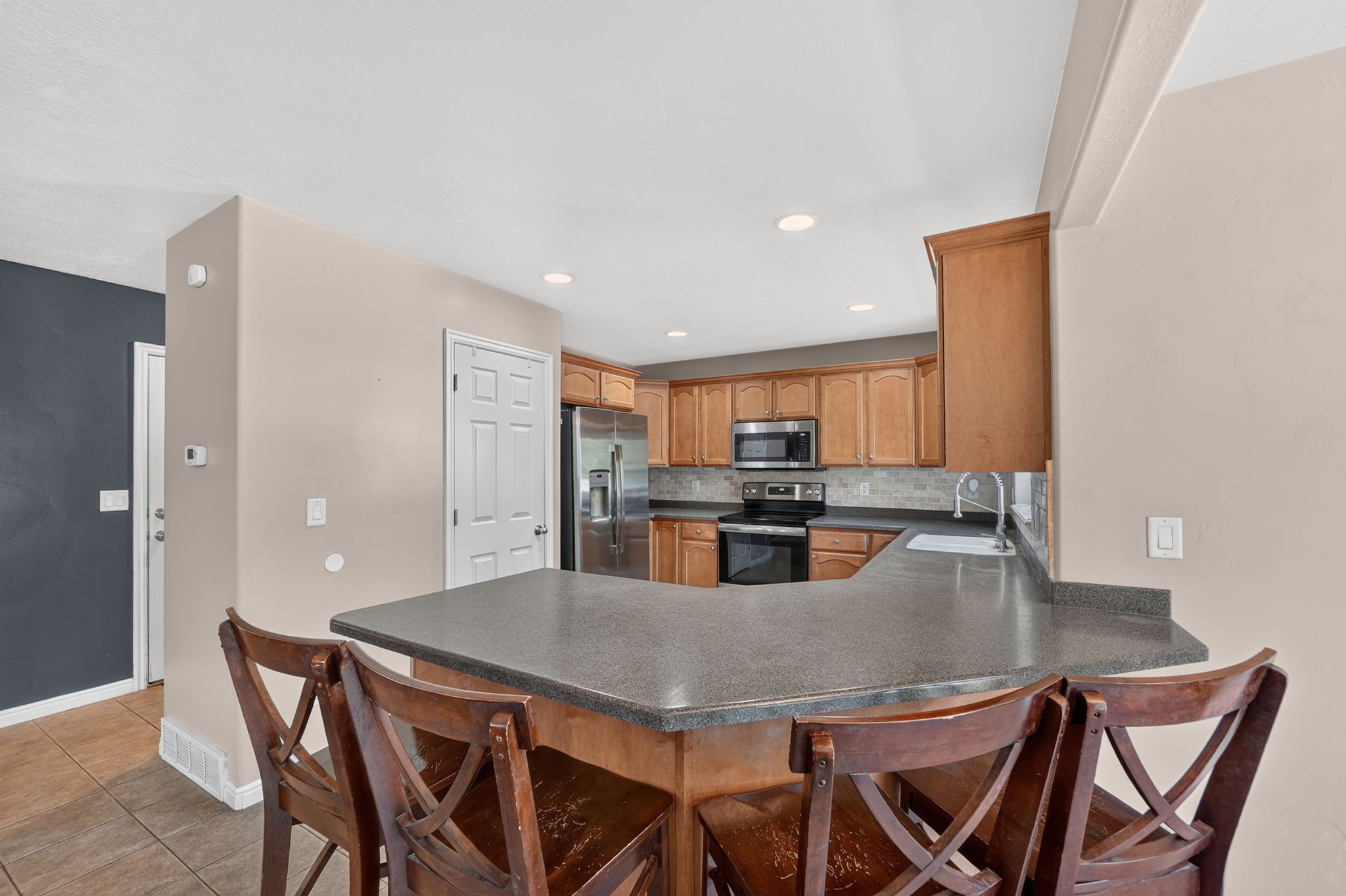 Kitchen featuring a U-shaped breakfast bar with a stone-finish countertop, recessed lighting, wood-finish cabinetry, stainless steel appliances, and a tile backsplash
