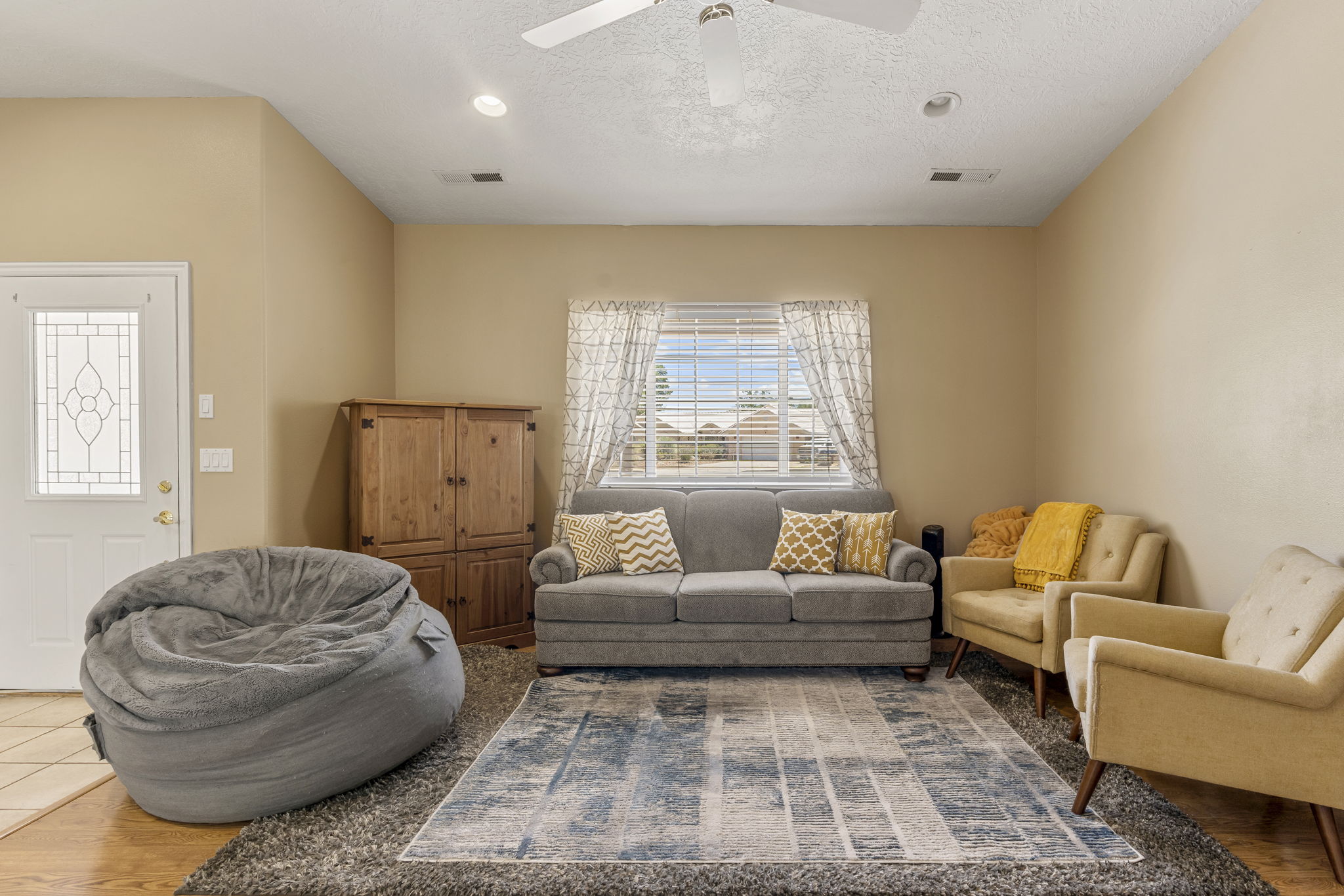 Spacious living area featuring neutral tone walls, wood-finish flooring, a decorative front door with opaque glass panels, a ceiling fan, and recessed lighting