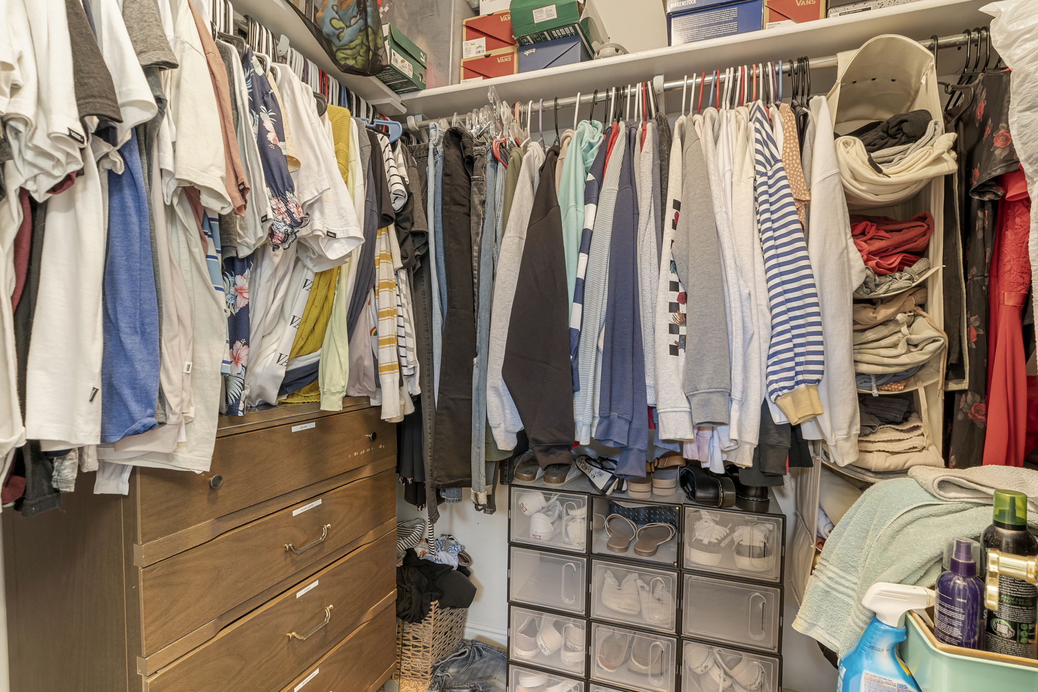 Closet featuring integrated shelving, multiple hanging rods, and a built-in wood-finish dresser