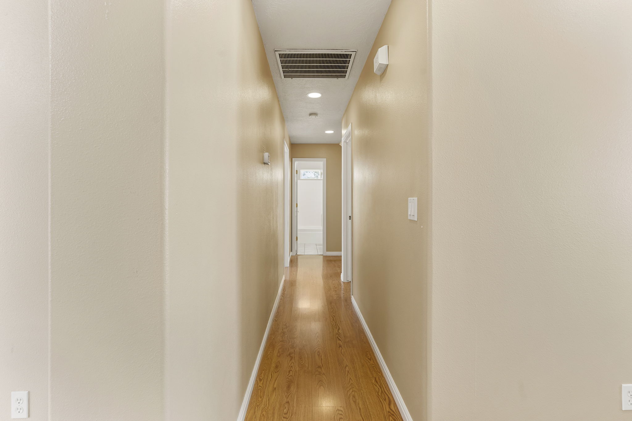 Long hallway with light wood-finish flooring, recessed lighting, and neutral wall tones
