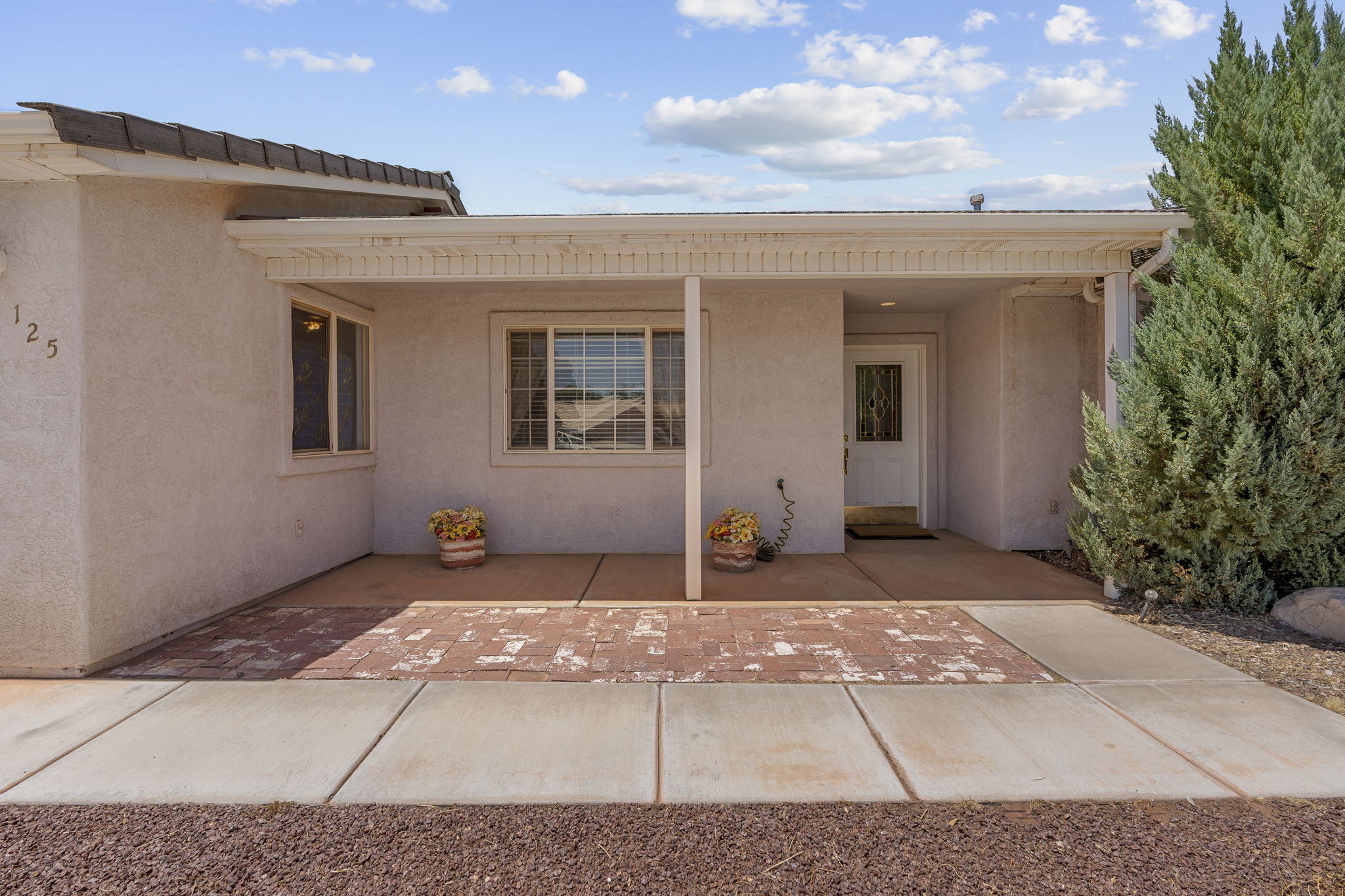 Stucco exterior featuring a covered front porch with brick paver accents and a tiled roofline