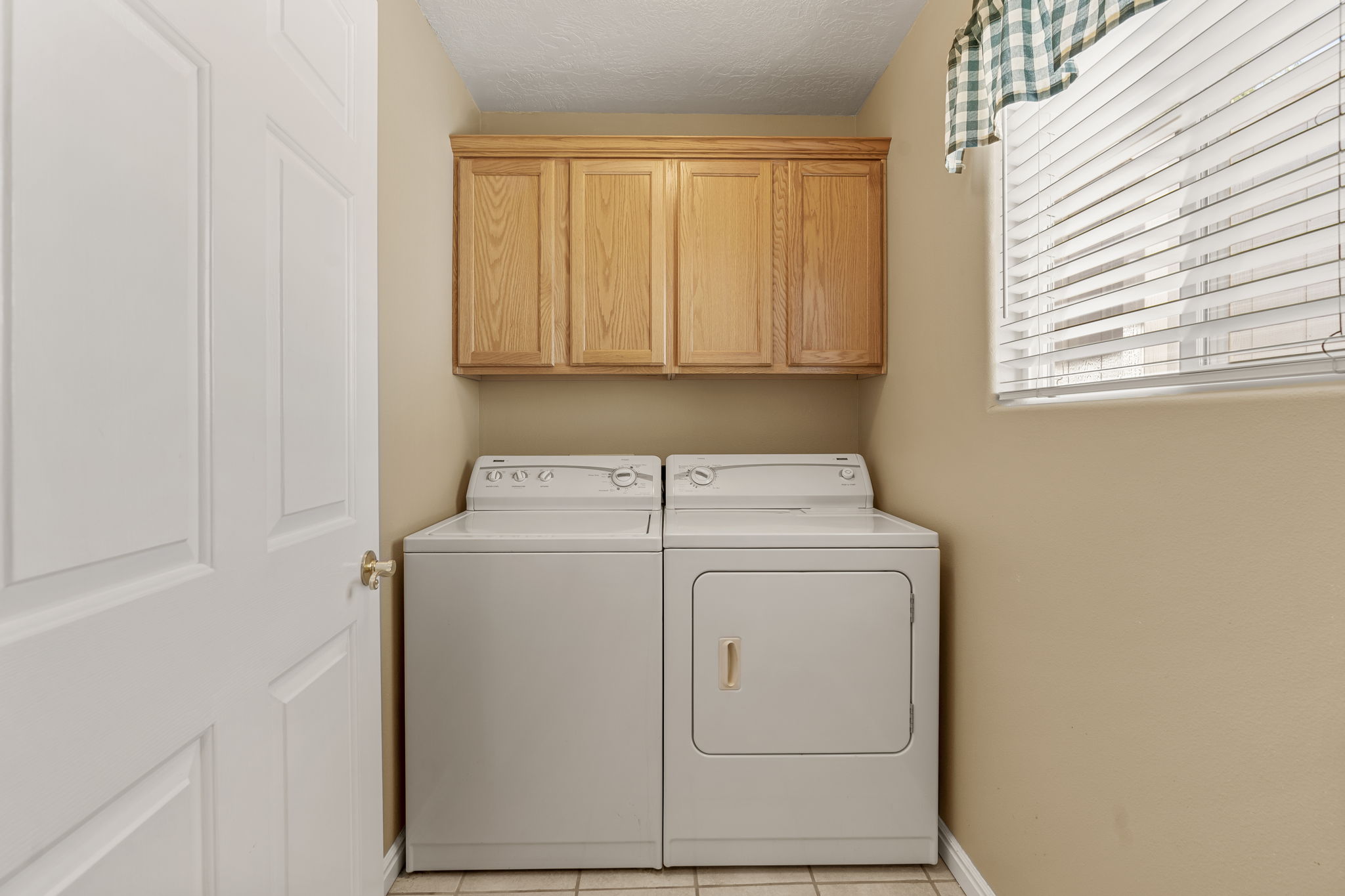 Utility area featuring a window with blinds, upper wood cabinetry, and neutral wall tones
