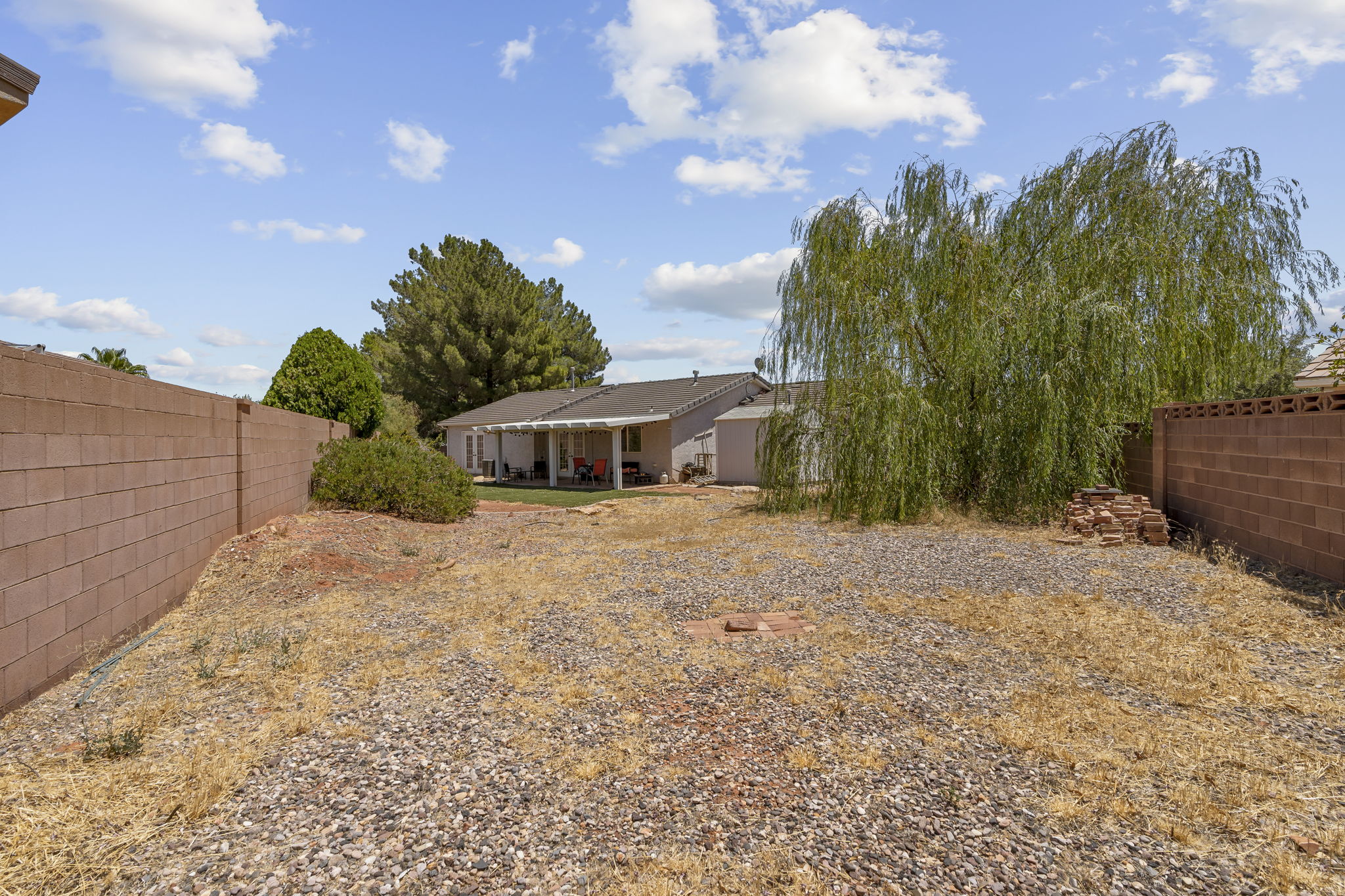 Expansive backyard featuring mature trees, a covered patio area, and perimeter block wall fencing
