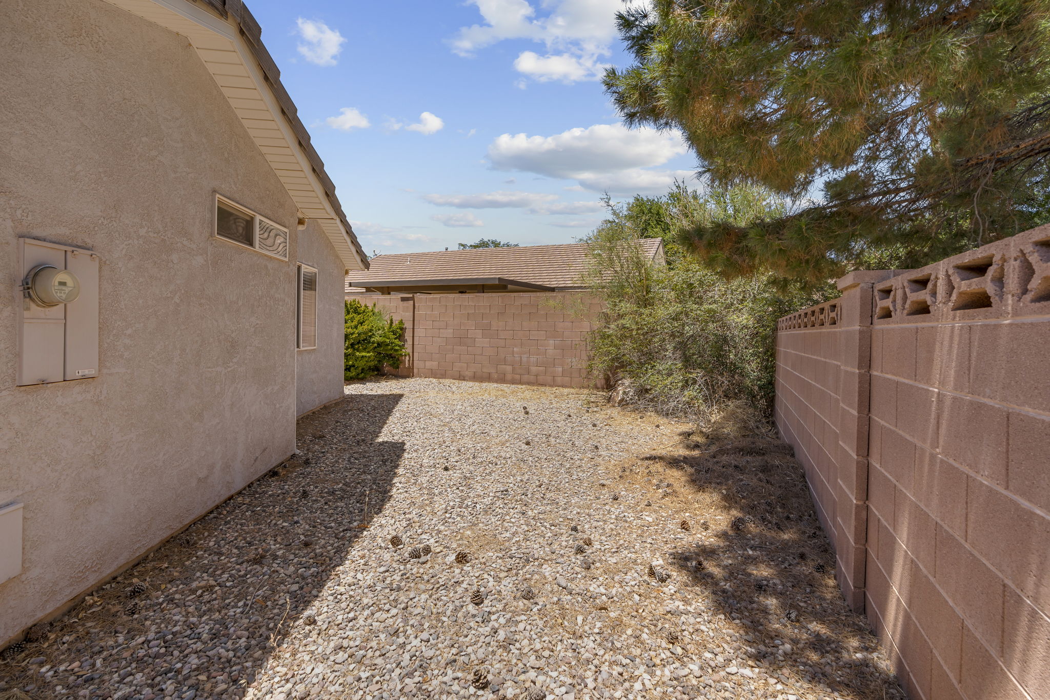 Side yard with gravel landscaping, a stucco exterior, and a block fence featuring decorative top elements