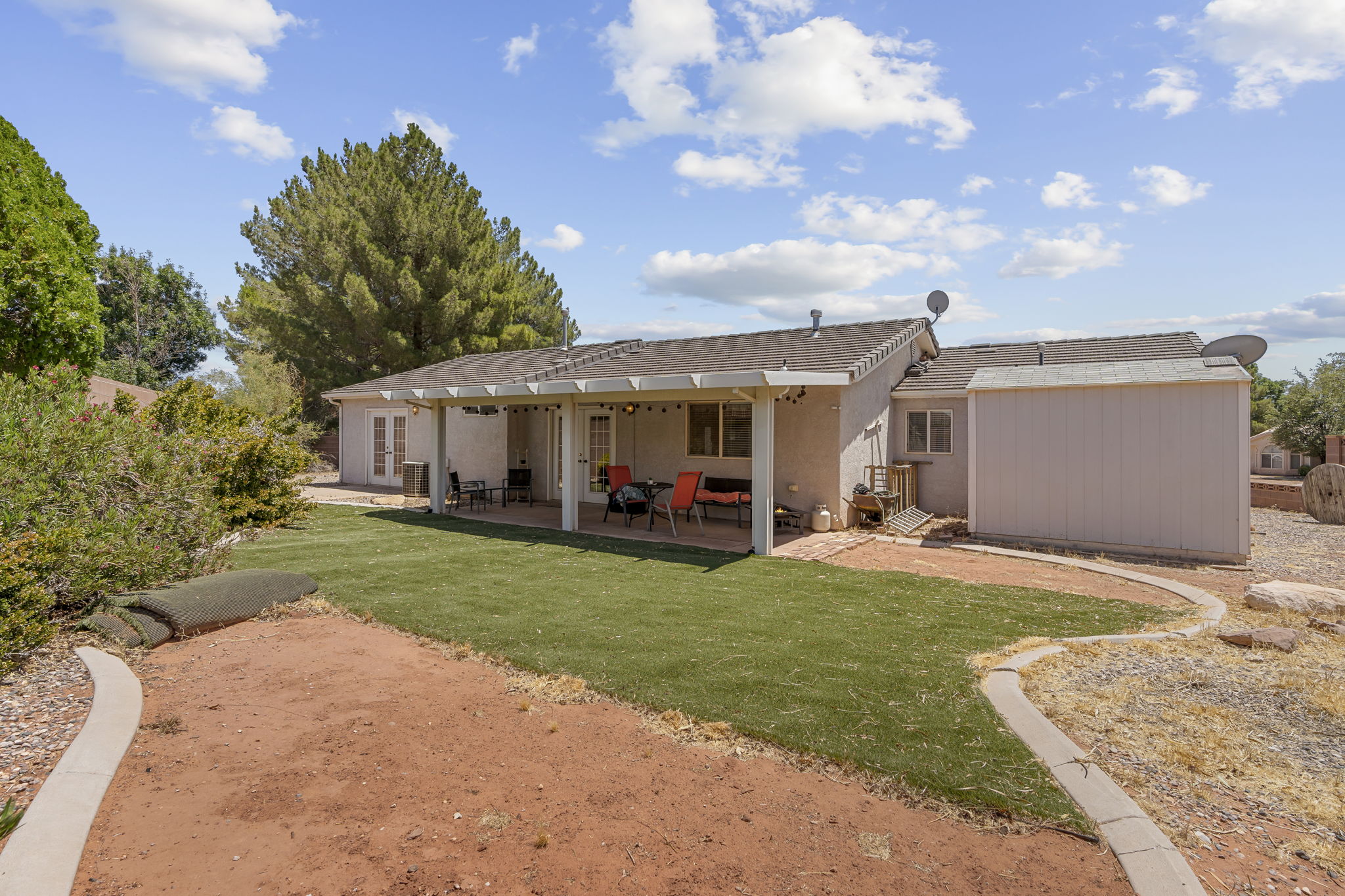 Expansive backyard featuring a covered patio, artificial turf, perimeter curbing, and a storage shed