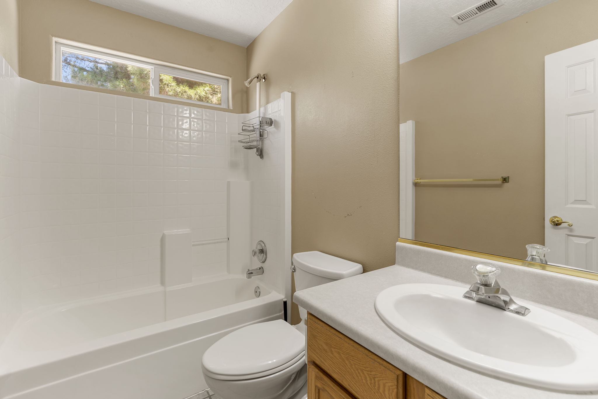 Full bathroom featuring a single vanity with wood-finish cabinetry and an integrated sink, a white toilet, and a white tub and shower combination with an overhead window