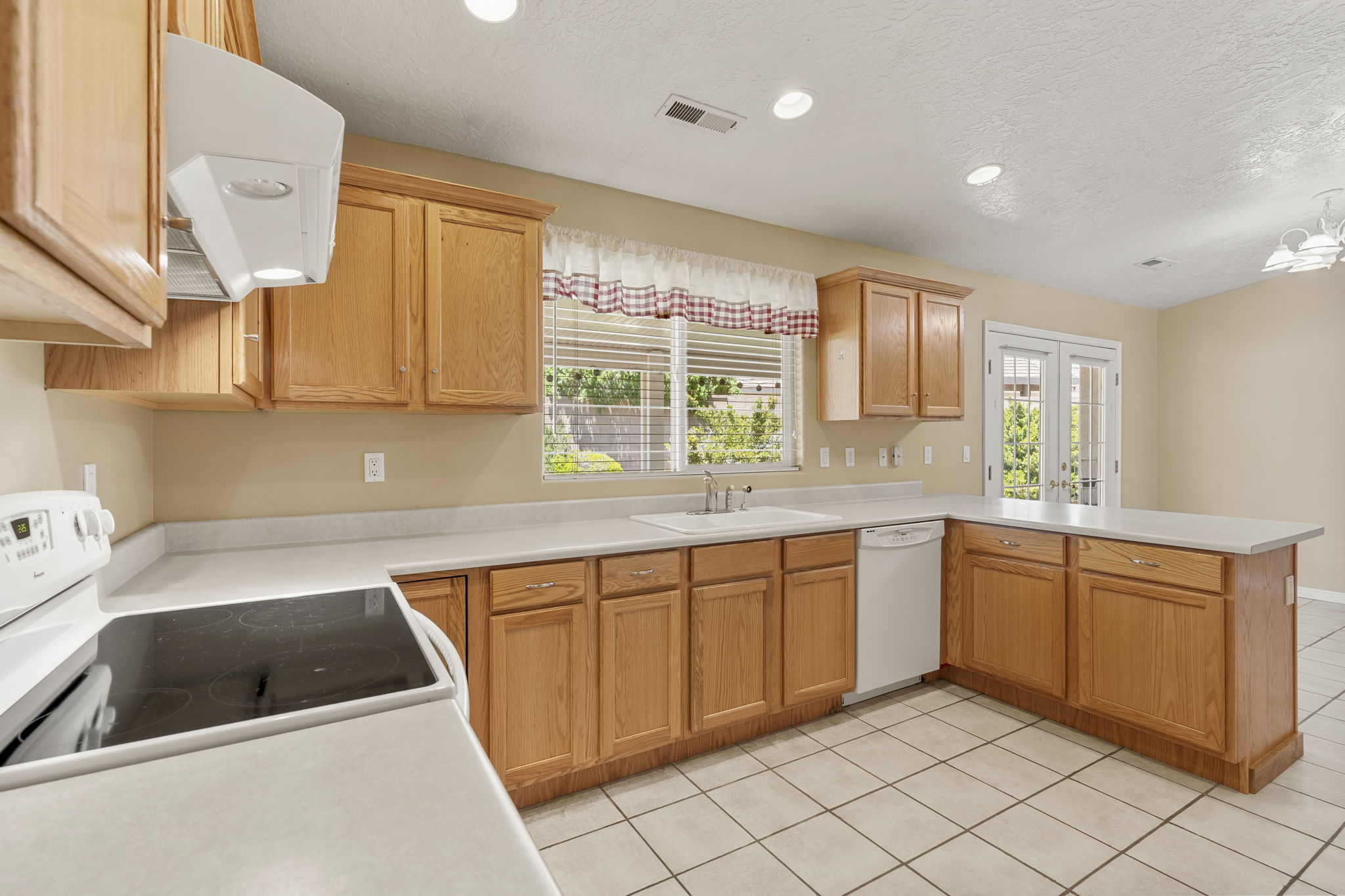 U-shaped kitchen featuring wood cabinetry, white countertops, a built-in electric range, a double basin sink, and tile flooring