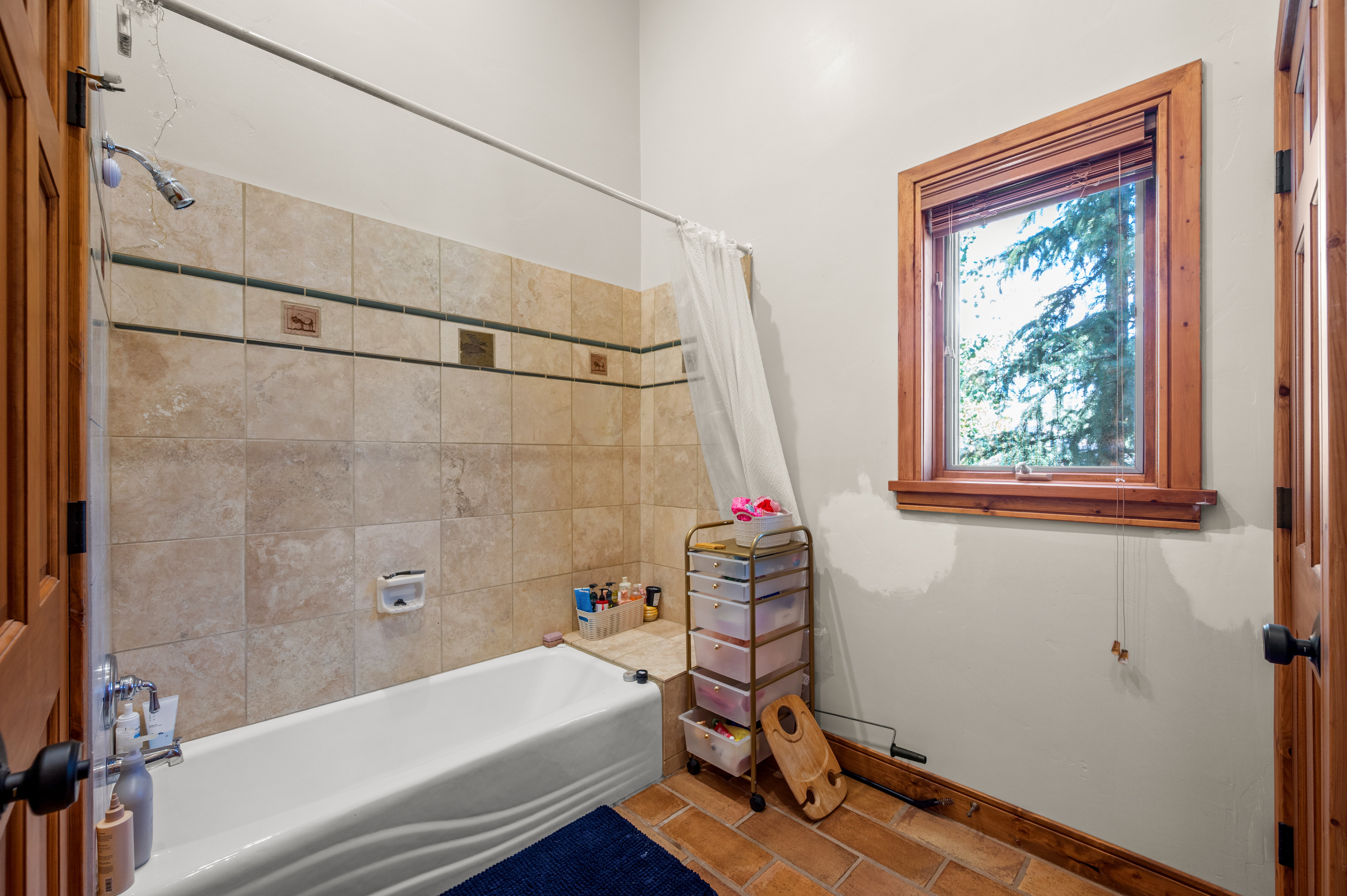 Bathroom featuring an alcove bathtub with tiled surround, a window with wood trim, and terracotta-style flooring
