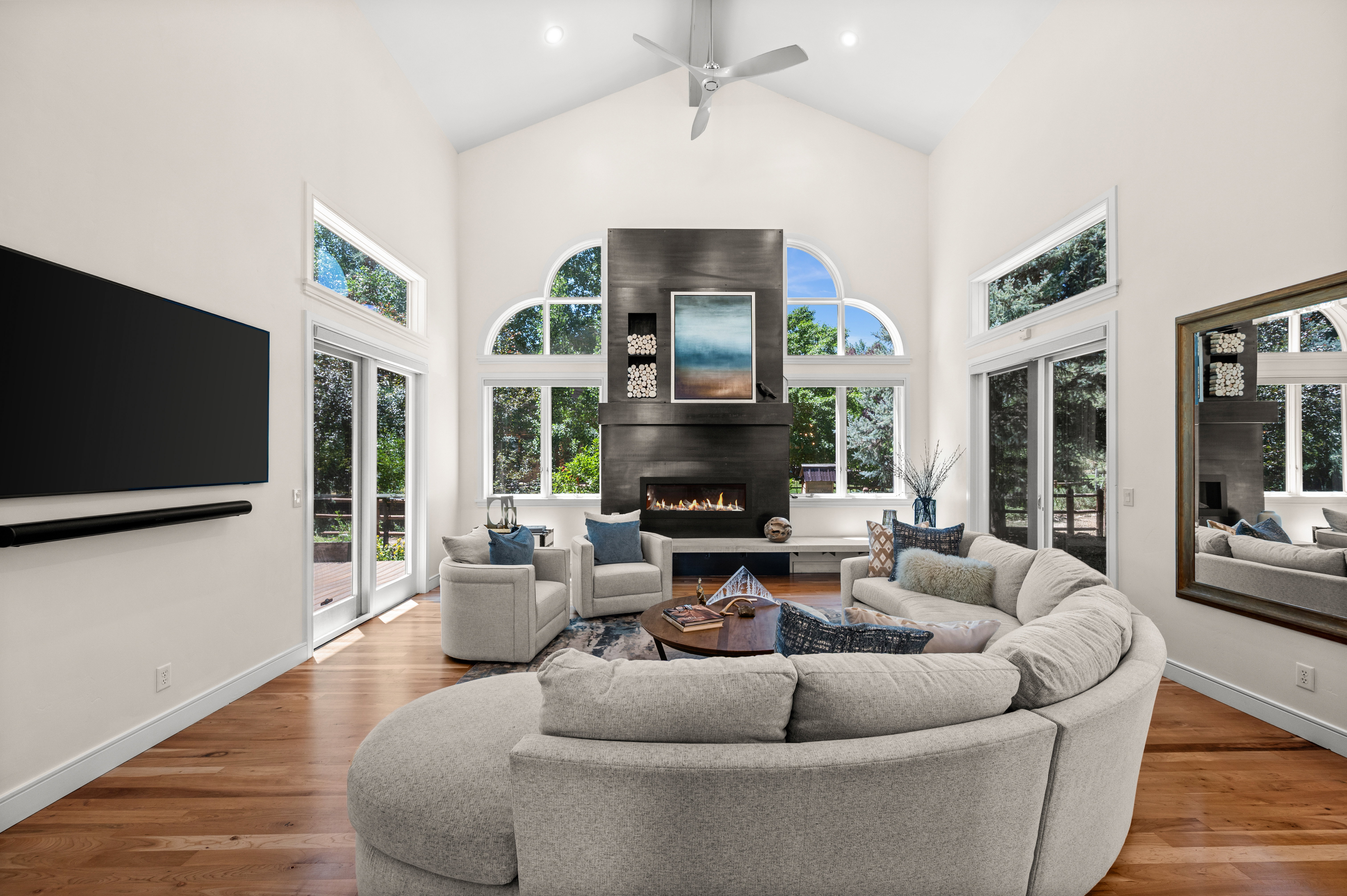 Spacious living area featuring a vaulted ceiling, floor-to-ceiling fireplace with an integrated linear fire feature, and multiple arched windows