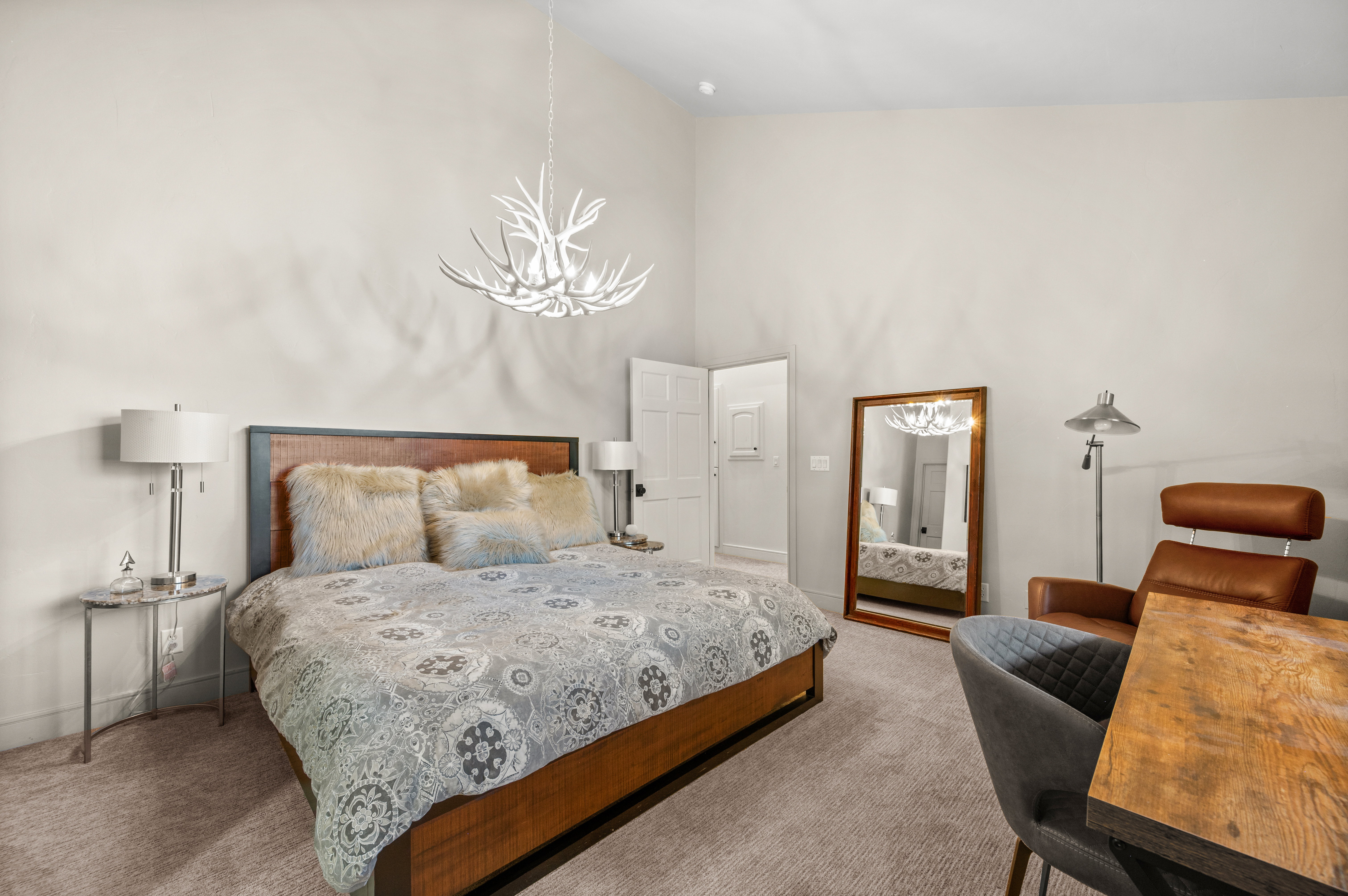Vaulted ceiling with a unique antler-inspired chandelier, light beige wall paint, textured carpeting, and a white paneled door