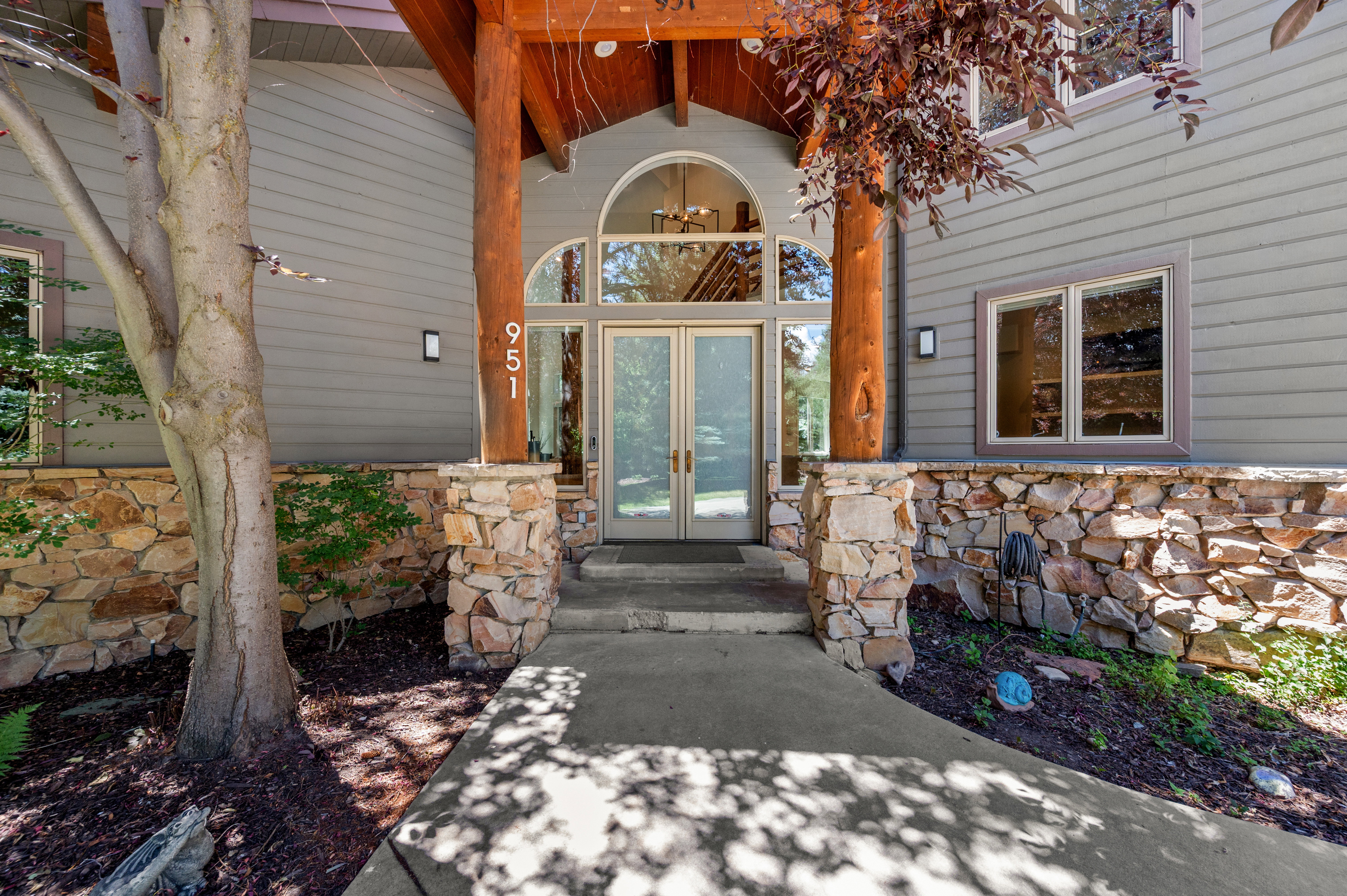 Grand entryway featuring double glass doors with an arched transom, flanked by robust wood columns and a stone-clad foundation
