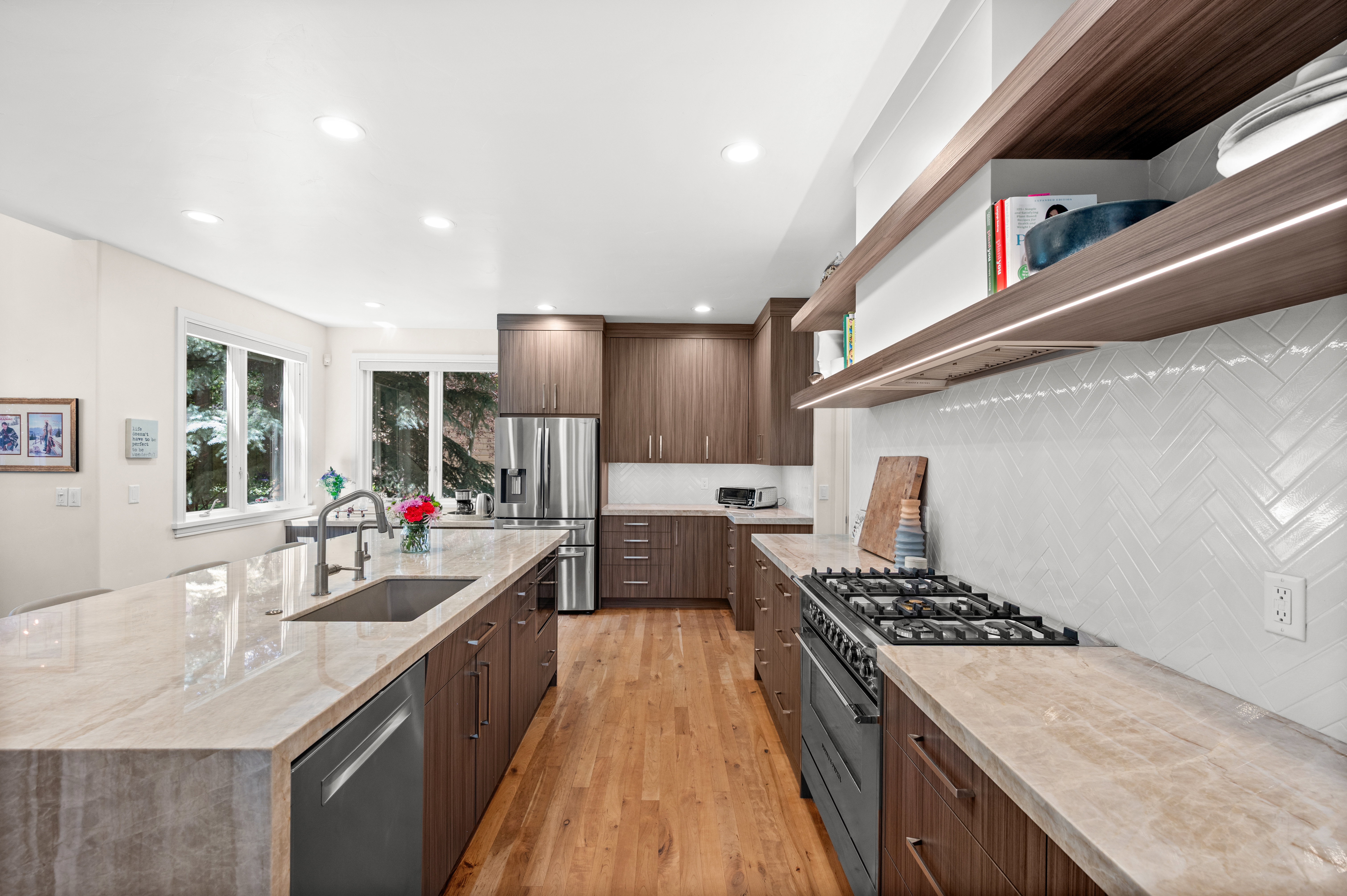 Gourmet kitchen featuring a large island with an undermount sink, stone countertops, wood-finish cabinetry, stainless steel appliances, and wood-finish flooring