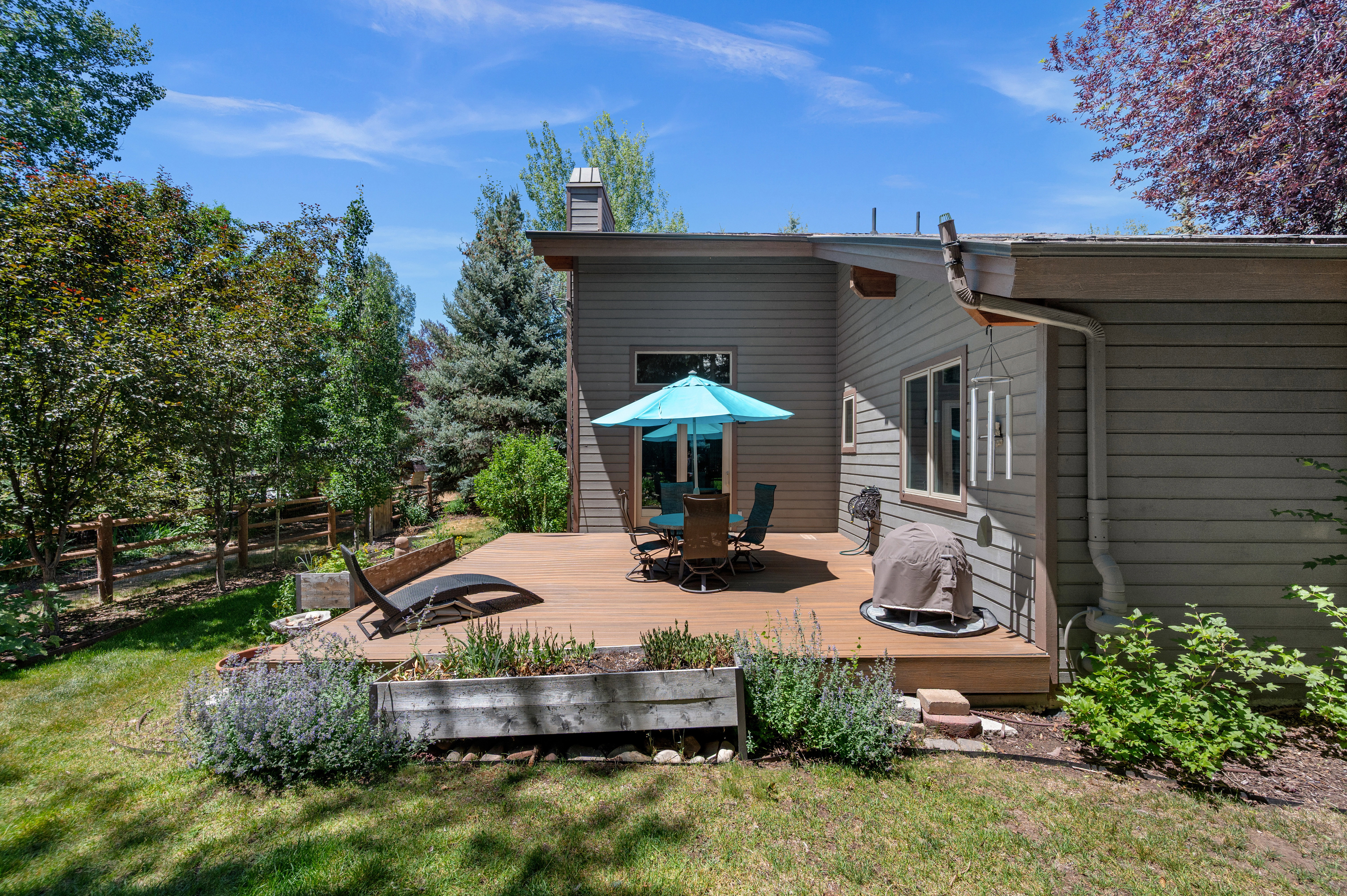 Spacious outdoor deck featuring wood-finish flooring, surrounded by lush greenery and mature trees