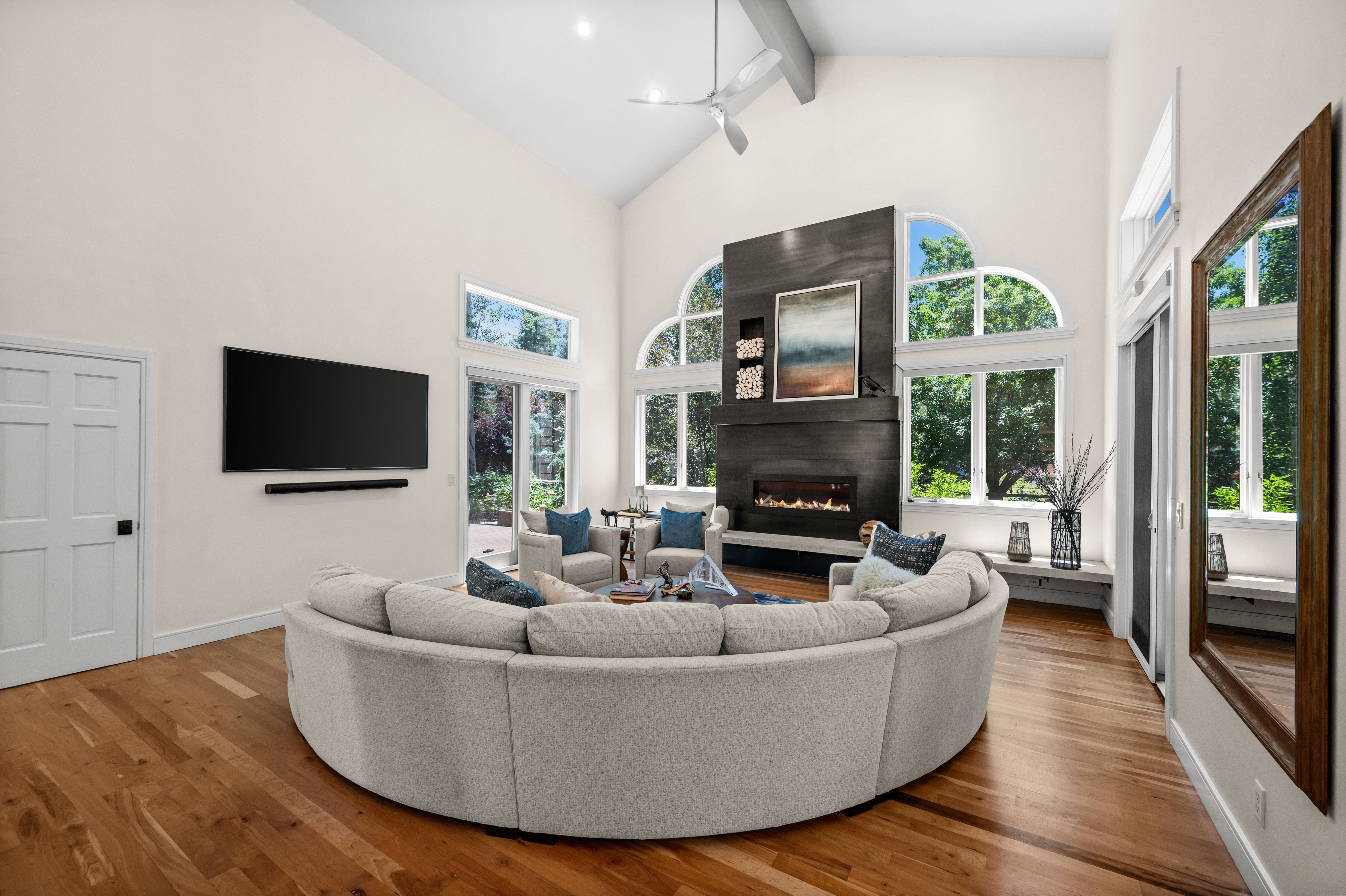 Spacious living area featuring vaulted ceilings, a modern fireplace with integrated shelving, and large arched windows