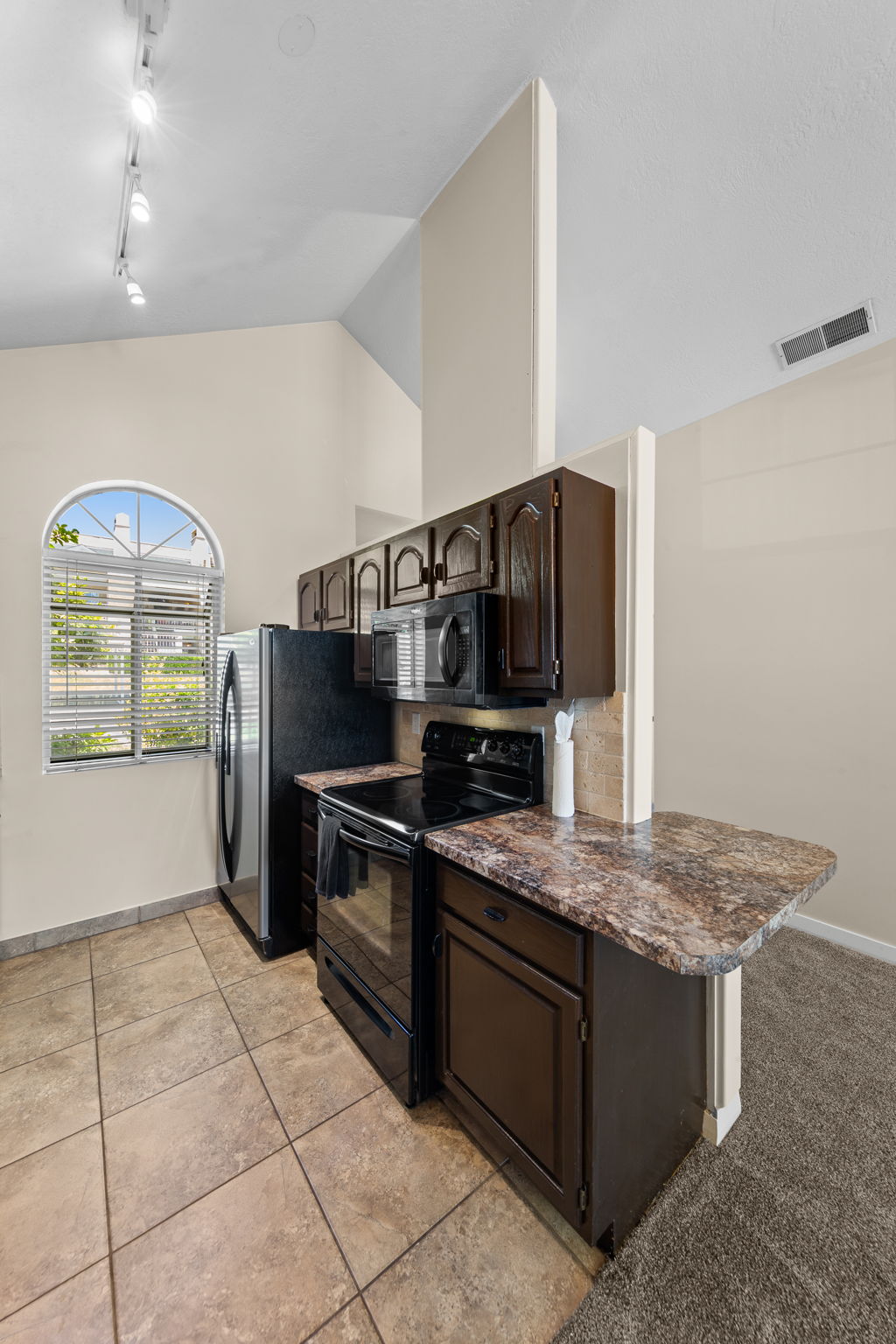 Kitchen featuring dark wood-finish cabinetry, black appliances, and a granite-finish countertop