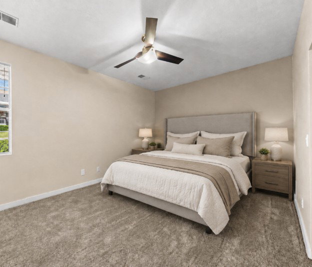Spacious bedroom featuring neutral carpeting, light-toned walls, a large window, a ceiling fan with integrated lighting, and white baseboards