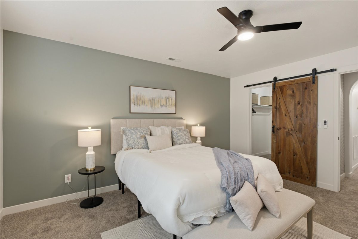 Bedroom featuring carpeting, a ceiling fan with integrated lighting, and a barn door entry to a closet with built-in shelving