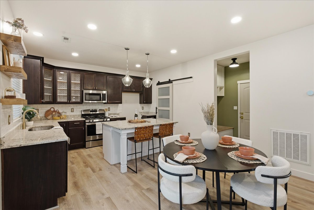Gourmet kitchen and dining area featuring dark wood cabinetry, stainless steel appliances, light granite countertops, a subway tile backsplash, and wood-finish flooring