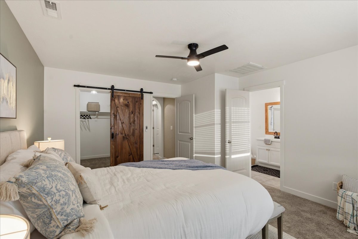 Spacious bedroom featuring carpet flooring, a barn door leading to a walk-in closet with built-in shelving, and direct access to an en-suite bathroom with a vanity and mirror