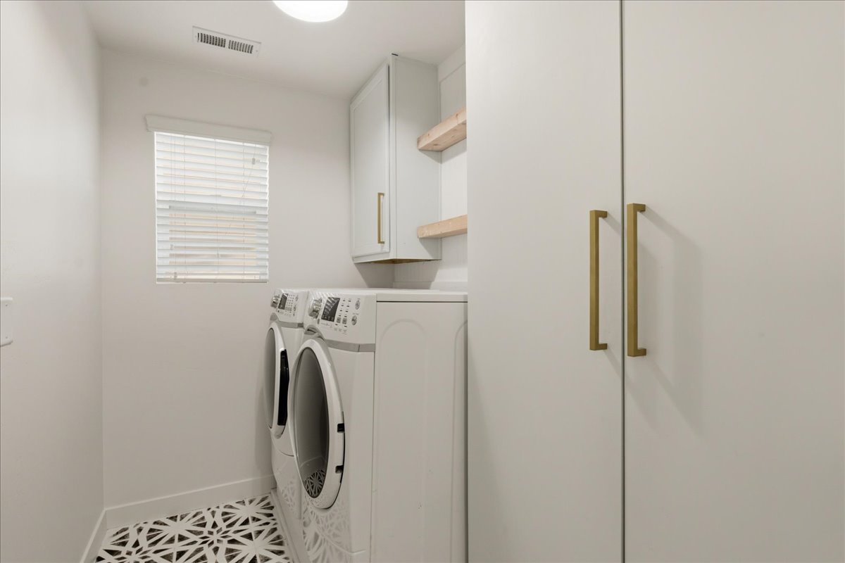 Laundry room featuring patterned floor tiles, light-colored cabinetry, and brass hardware