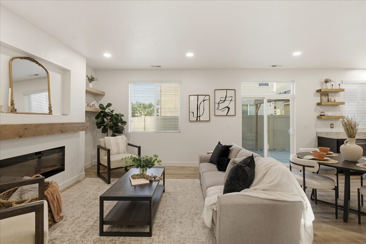Open-concept living space featuring wood-finish flooring, a contemporary fireplace with a substantial wood mantel, recessed lighting, and sliding glass doors to the exterior