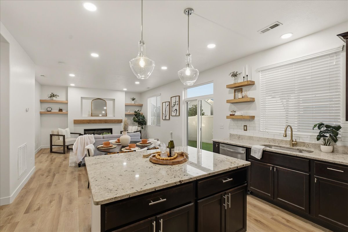 Kitchen island featuring a light granite countertop with pendant lighting, dark wood cabinetry, and wood-finish flooring throughout