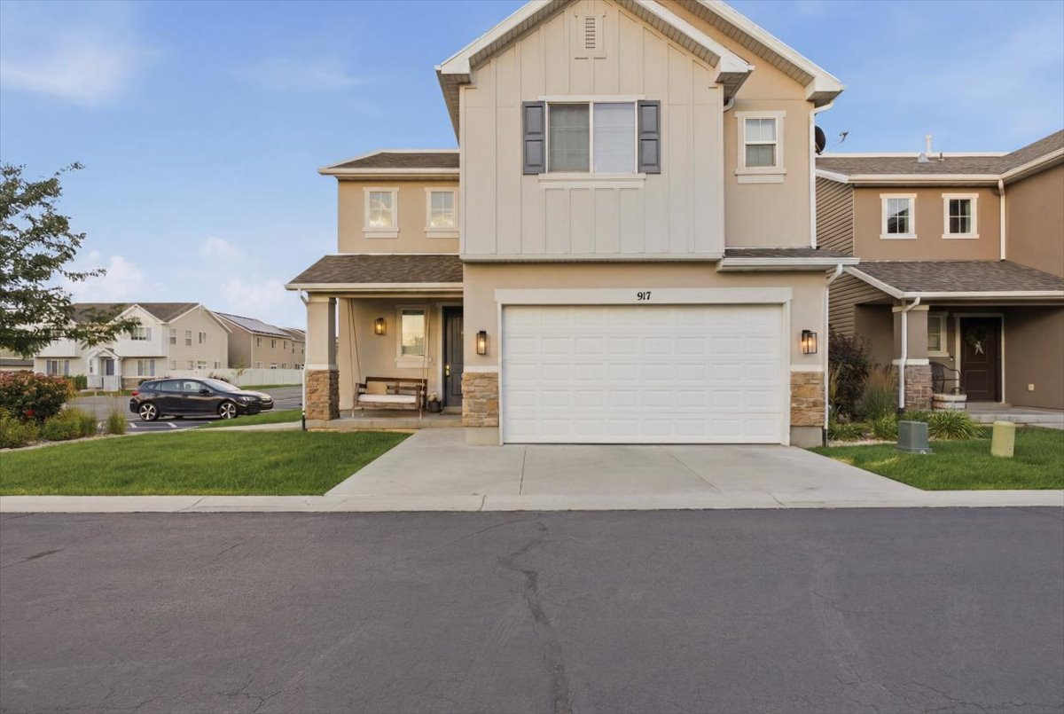 Contemporary townhome exterior featuring an attached two-car garage, covered porch entry, stacked stone accents, and a well-maintained lawn