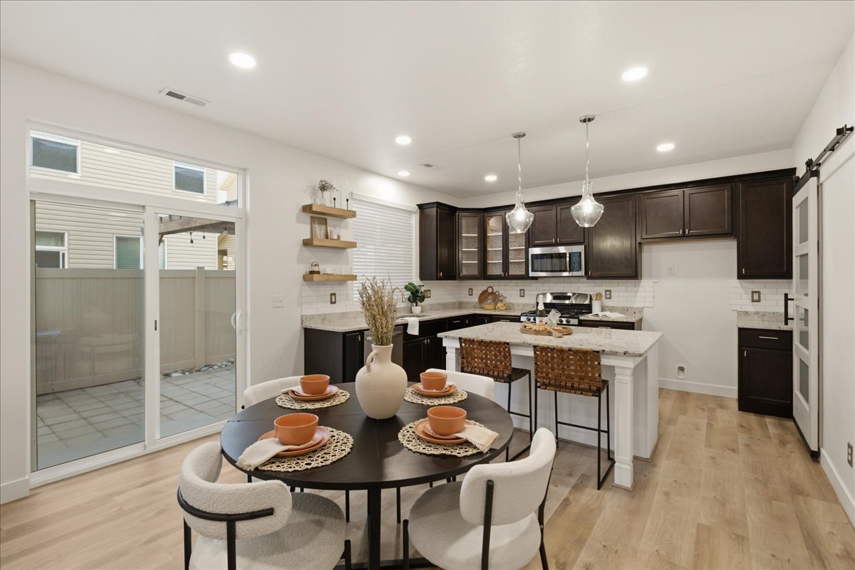 Kitchen and dining area featuring light wood-finish flooring, dark cabinetry, and a white subway tile backsplash