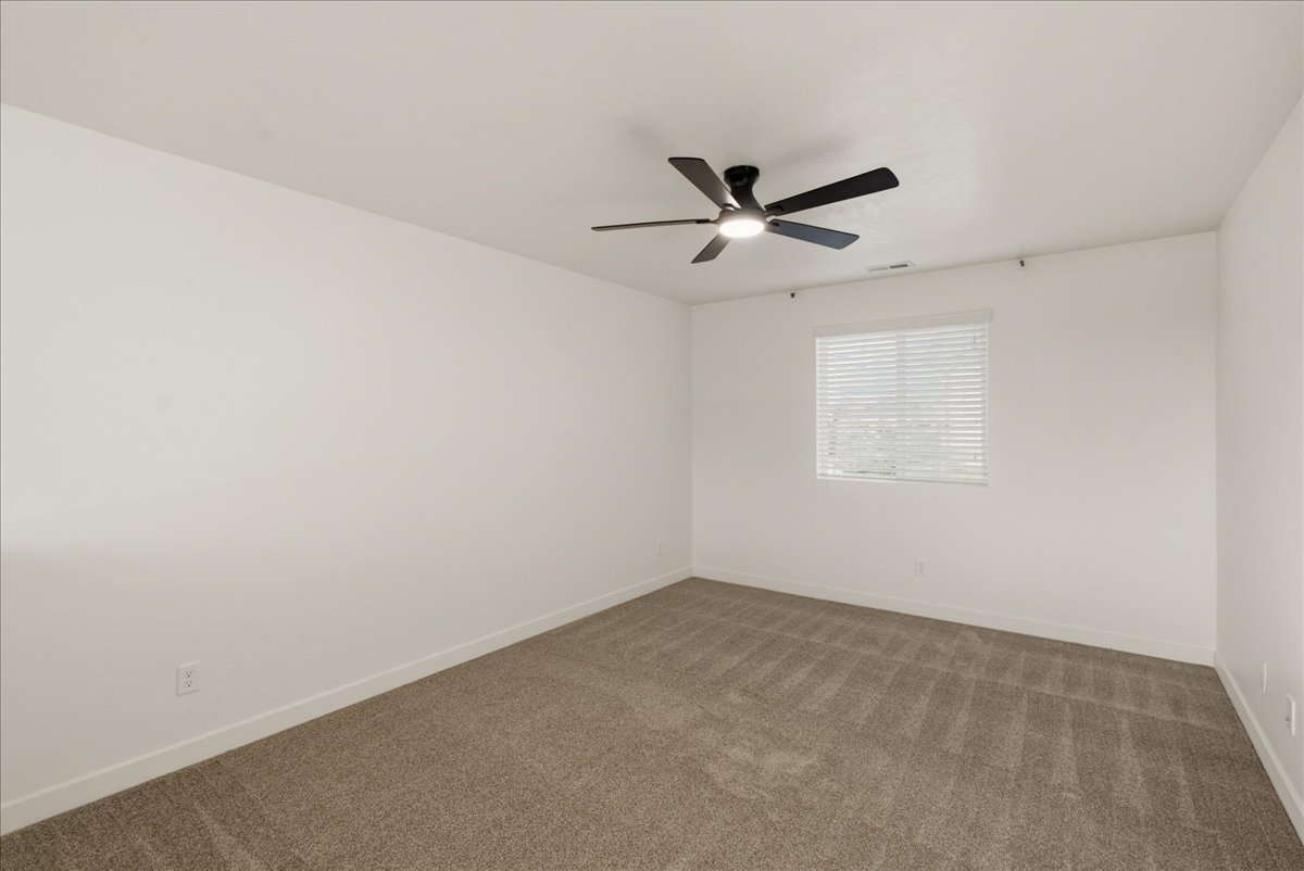 Spacious room featuring neutral carpeting, white baseboards, and a modern ceiling fan with integrated lighting