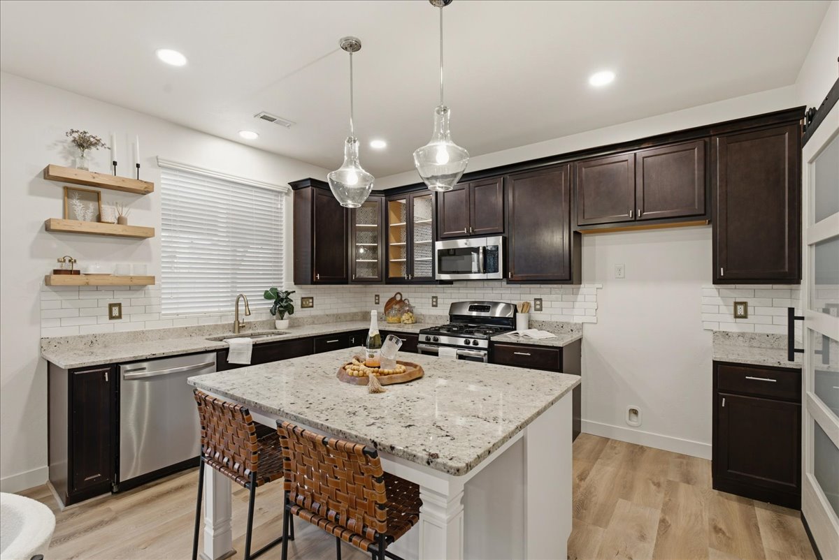 Spacious kitchen featuring an island with stone countertop, stainless steel appliances, dark wood cabinetry, white subway tile backsplash, and wood-finish flooring