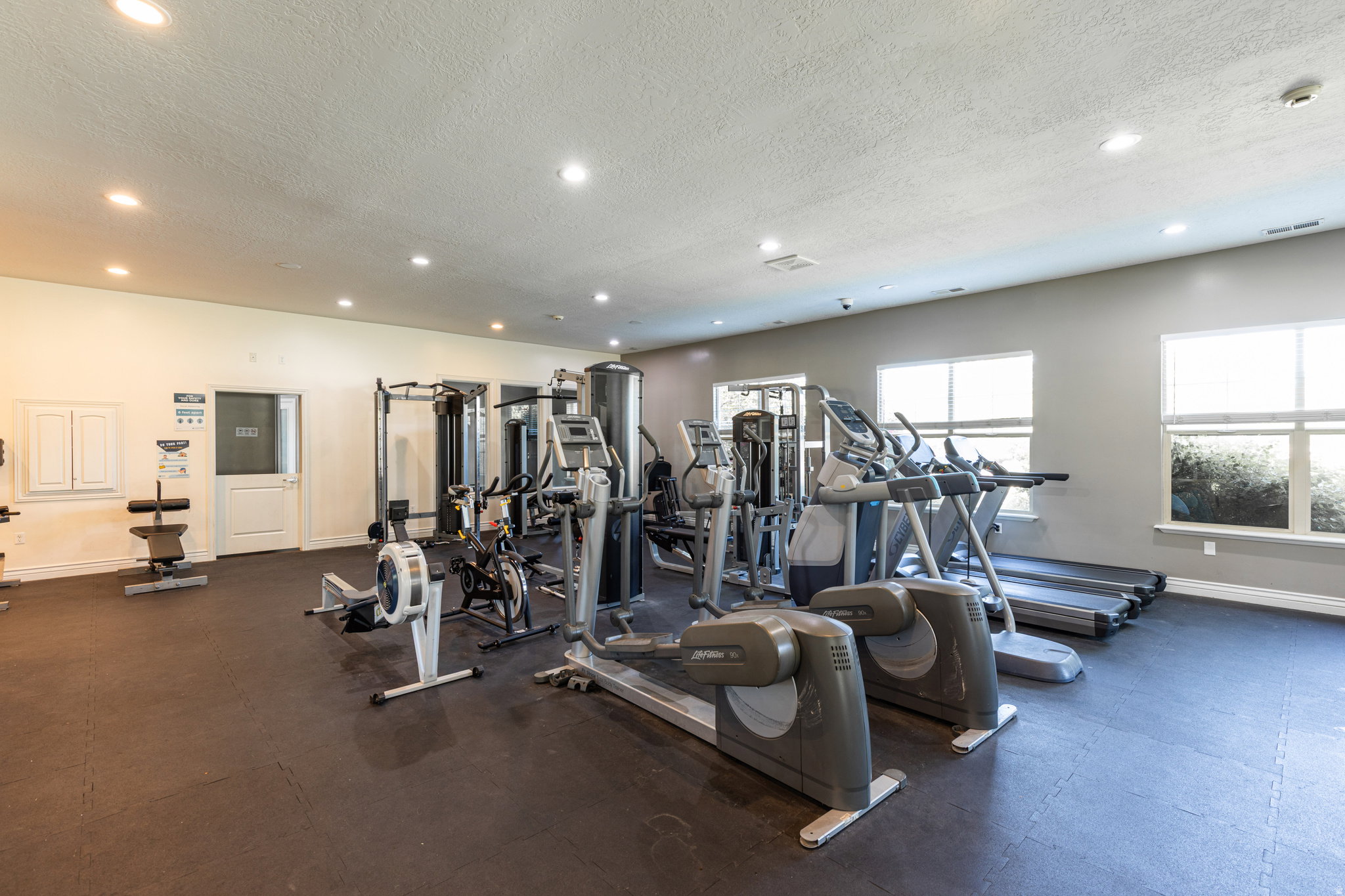 Fitness center featuring a variety of exercise equipment, recessed lighting, multiple windows, and durable rubber flooring