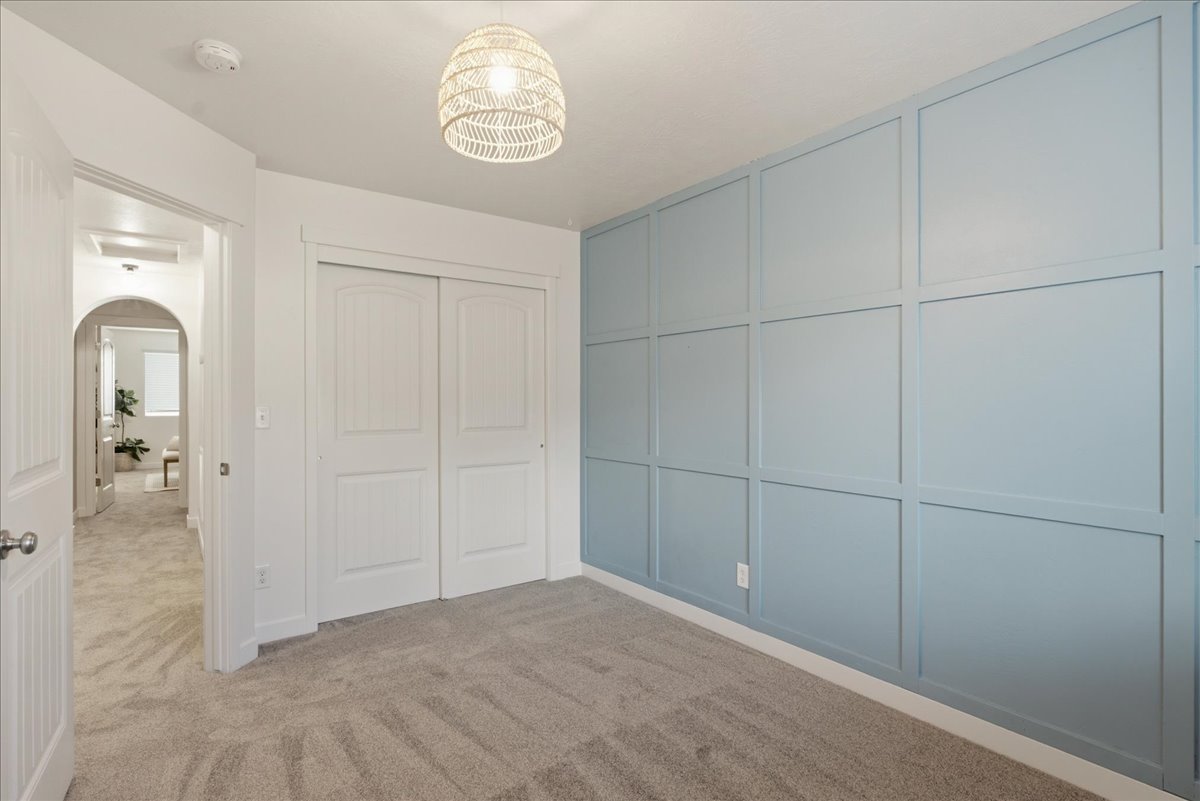Room featuring a decorative accent wall with blue paneling, light gray carpeting, and a woven pendant light fixture