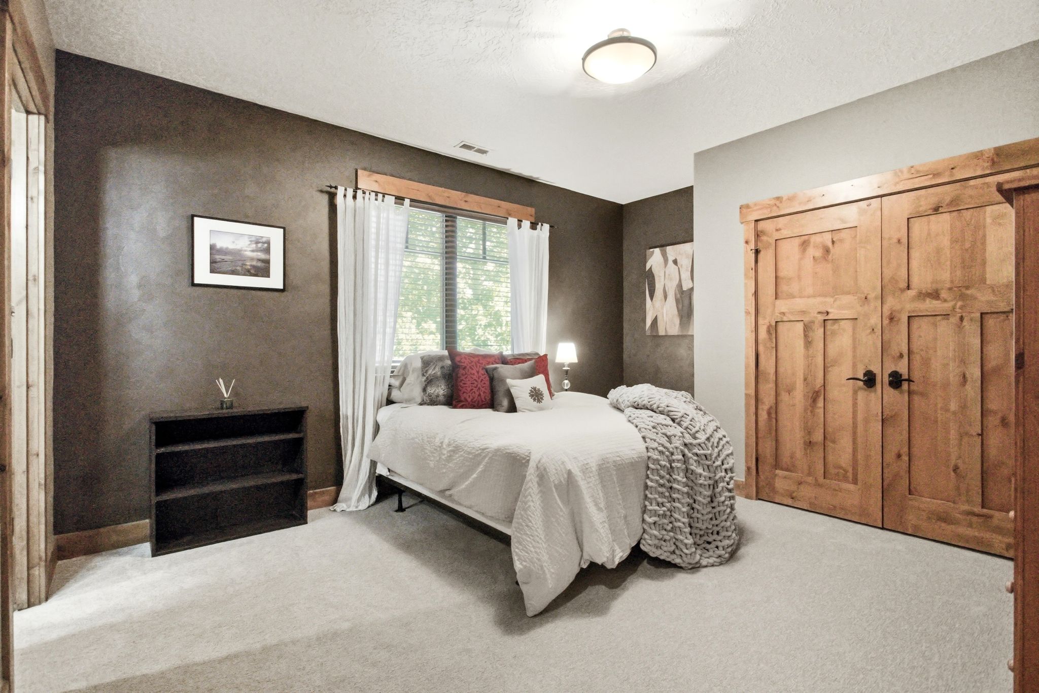 Bedroom featuring light-toned carpeting, wood-paneled closet doors, and wood trim around the window and doorways