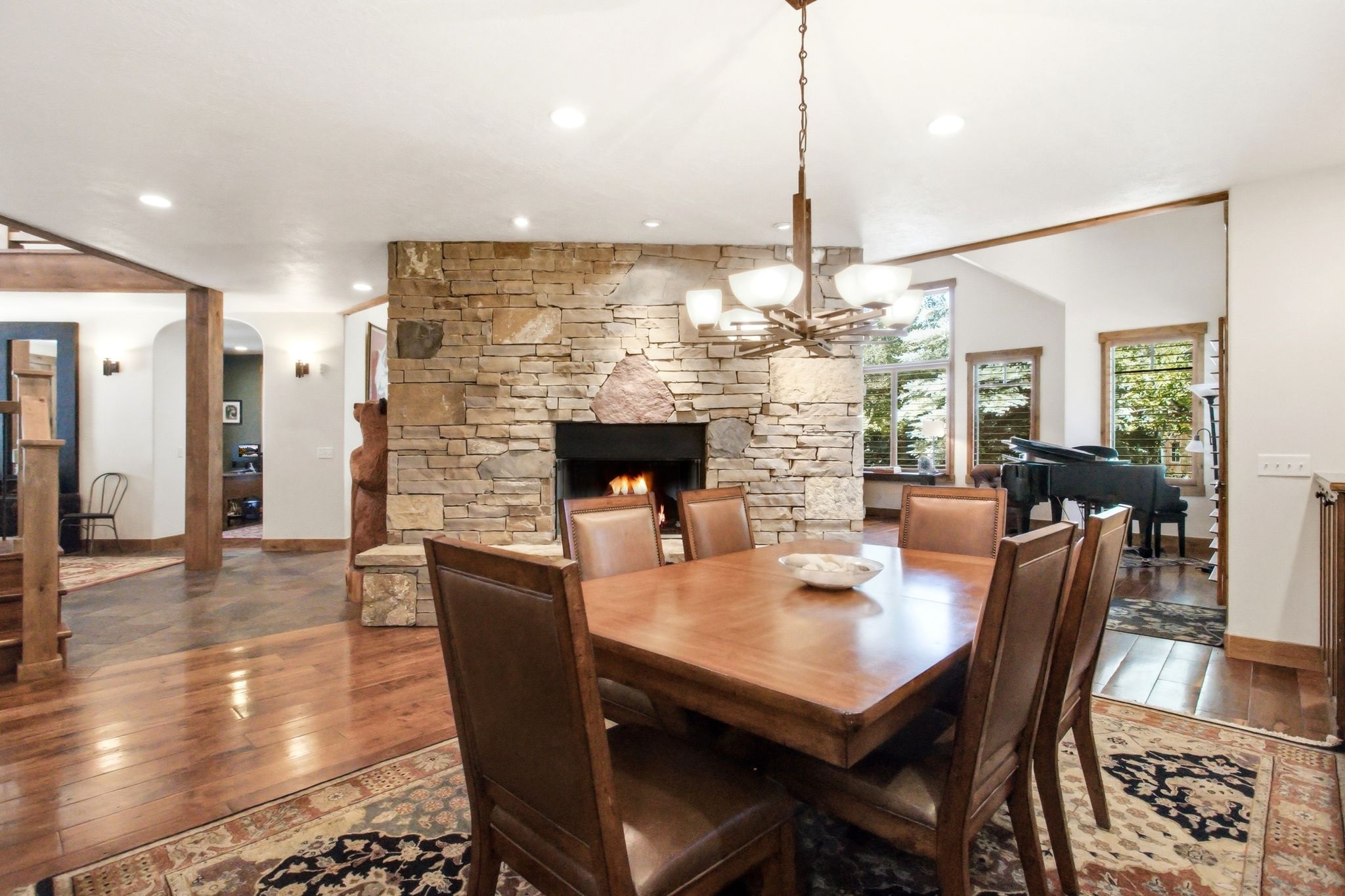 Spacious dining area featuring a stacked stone fireplace, hardwood flooring, and a chandelier