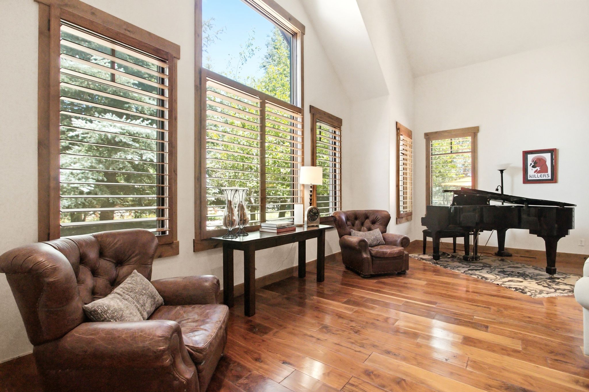 Spacious room featuring vaulted ceilings, large windows with natural wood trim, light-filtering horizontal blinds, and wood-finish flooring