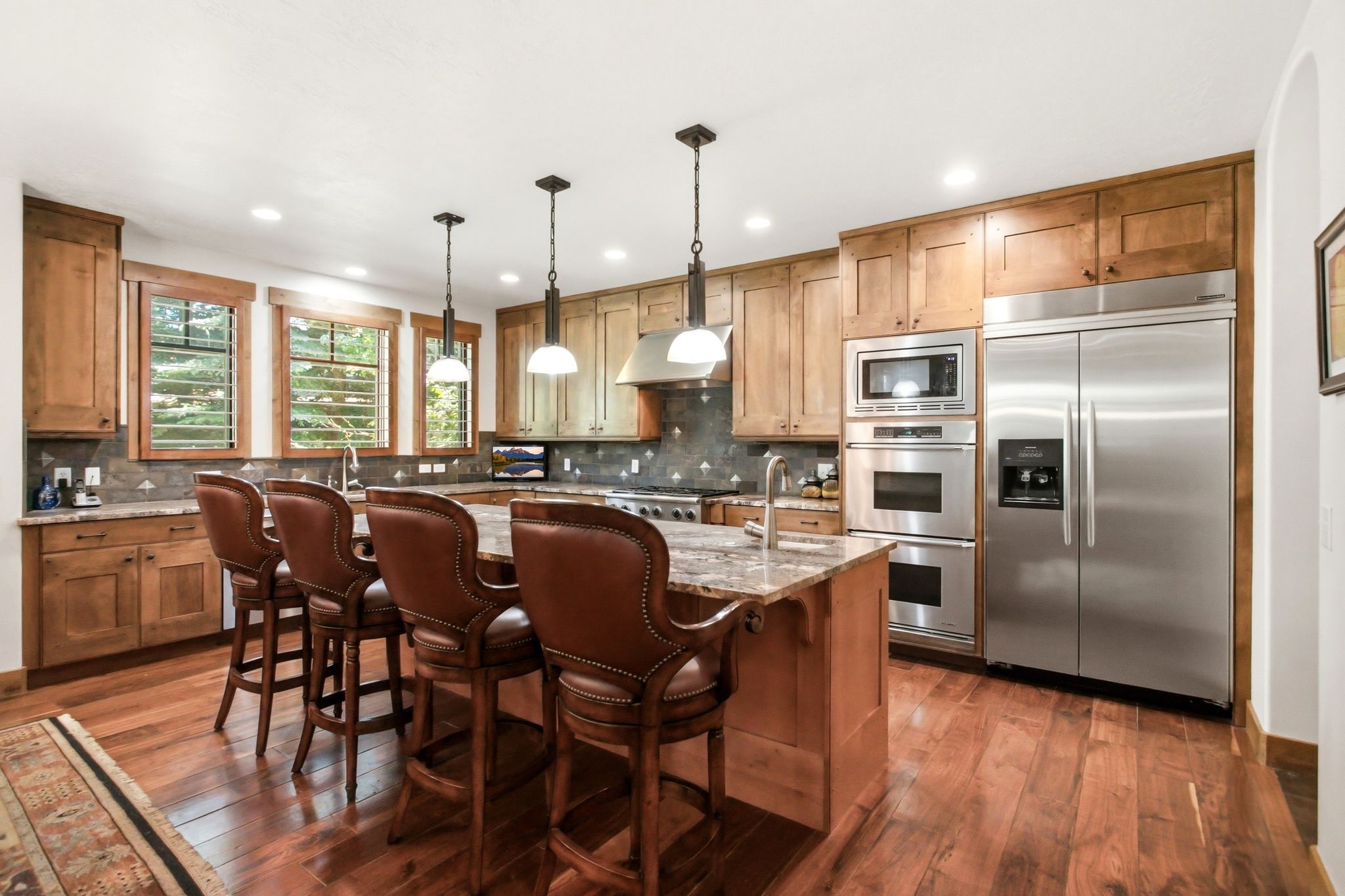 Gourmet kitchen featuring a substantial central island with seating, warm wood cabinetry, stainless steel appliances, and wood-finish flooring