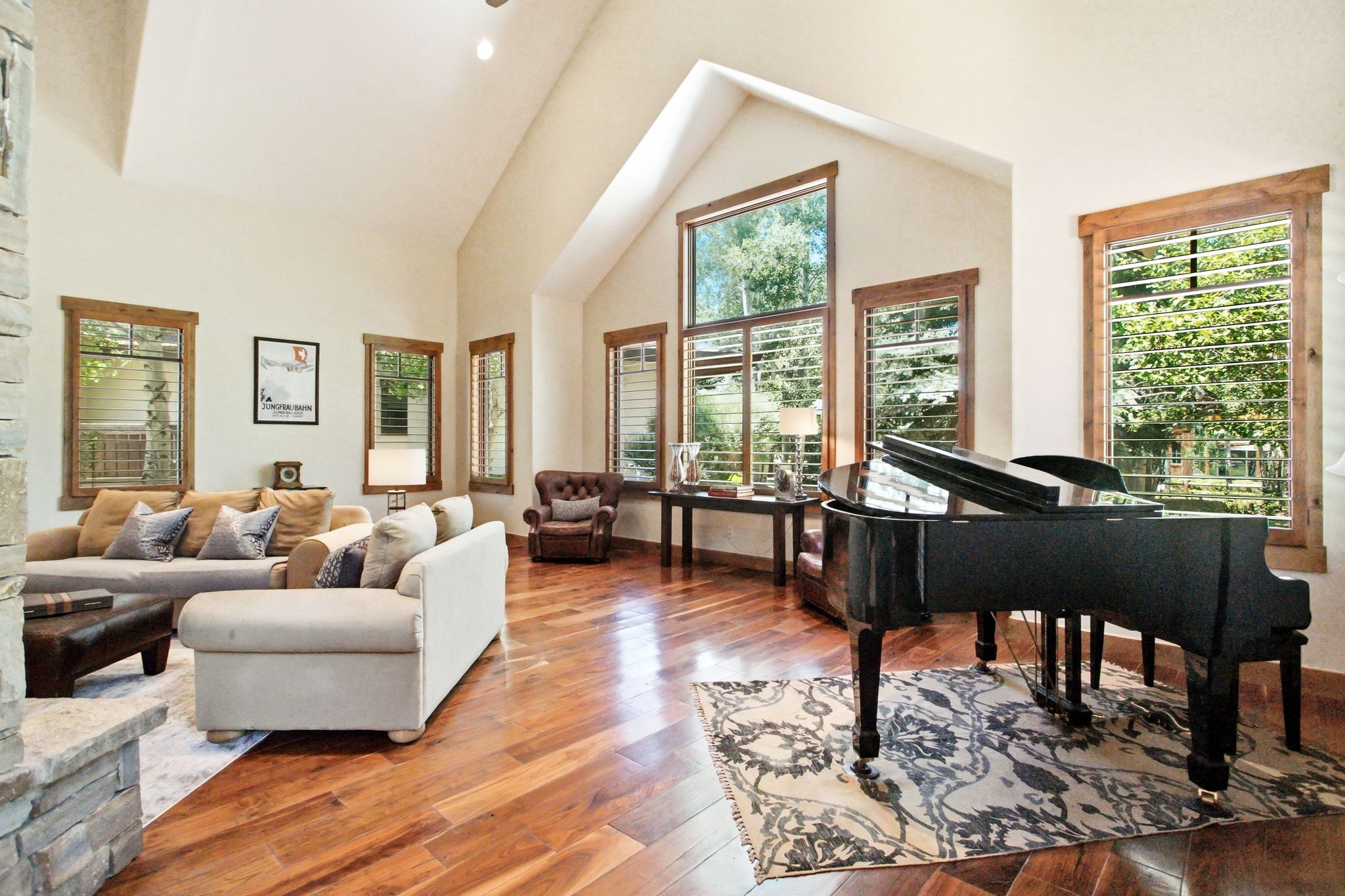 Spacious living area featuring high vaulted ceilings, warm wood-finish flooring, and multiple large windows with natural wood trim
