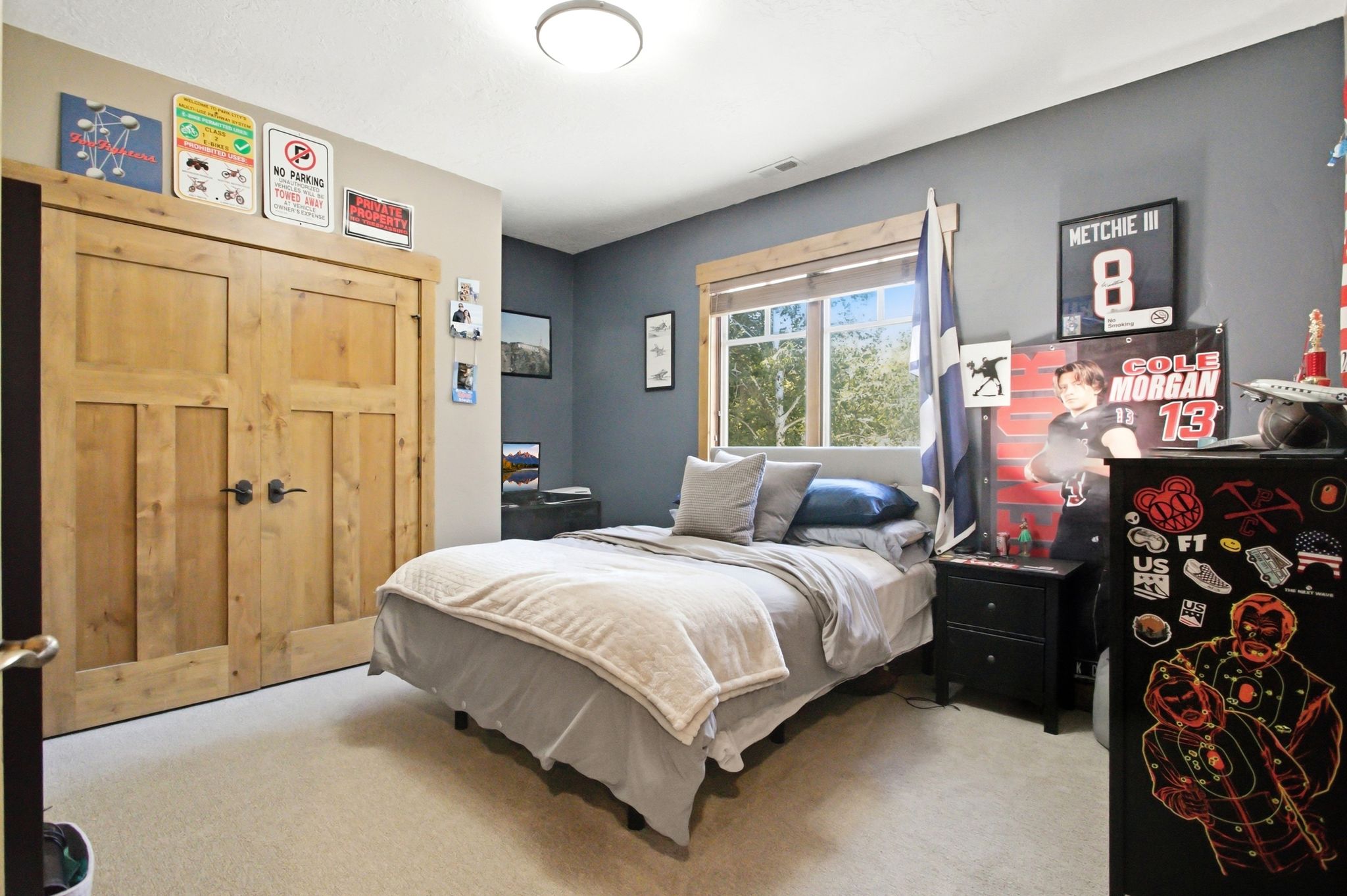 Carpeted room featuring a double-pane window with wood trim, a built-in closet with natural wood doors and matte black hardware, and a semi-flush ceiling light fixture