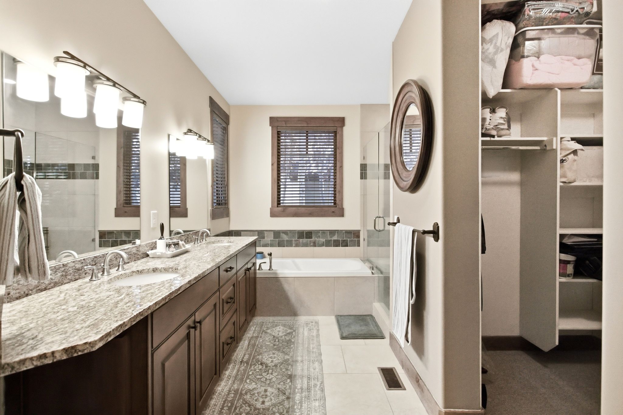 Bathroom featuring a dual vanity with a patterned countertop, a built-in bathtub, and an integrated walk-in closet with shelving
