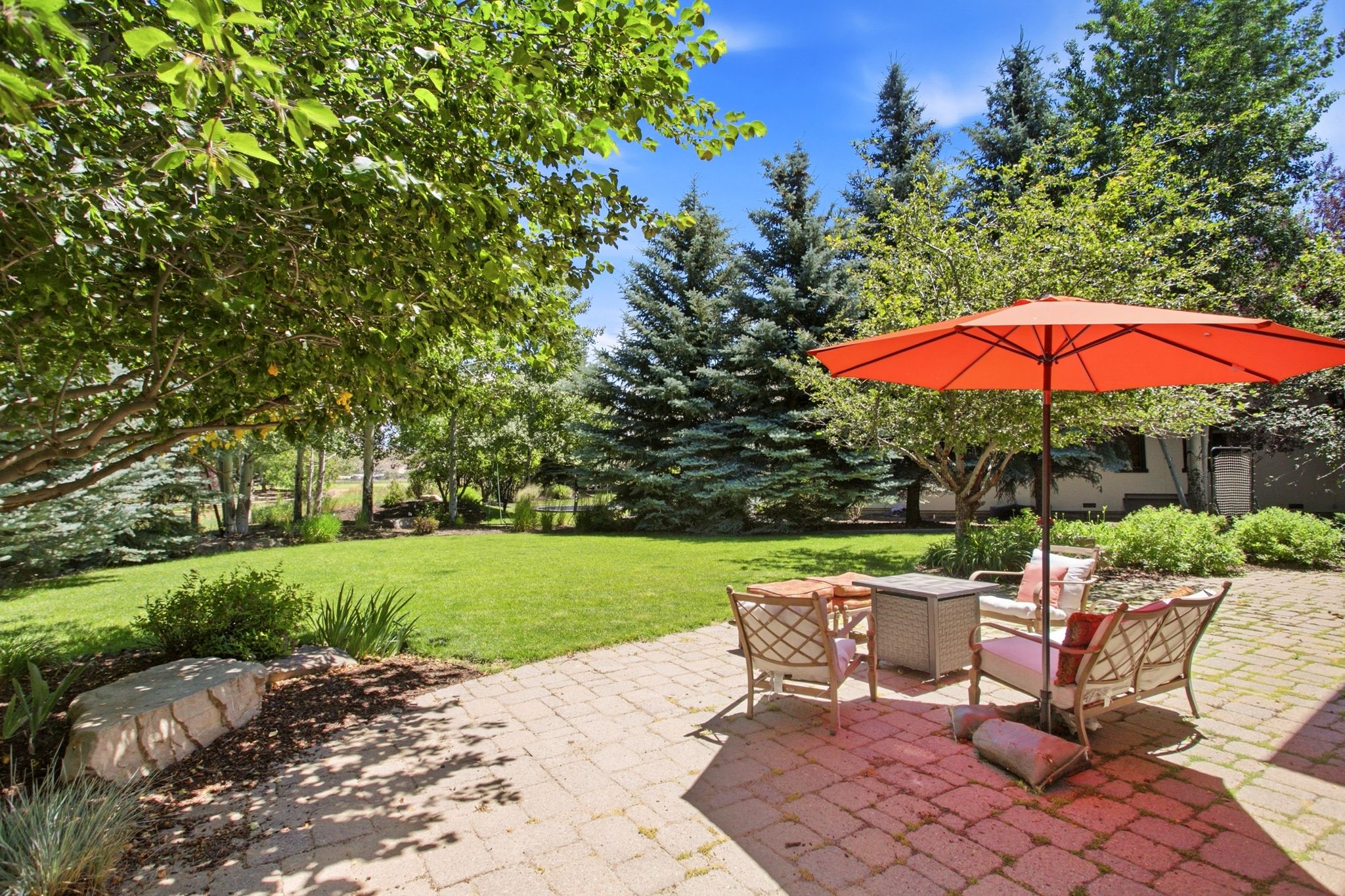 Spacious paver patio opens to a manicured lawn framed by mature trees and evergreen landscaping