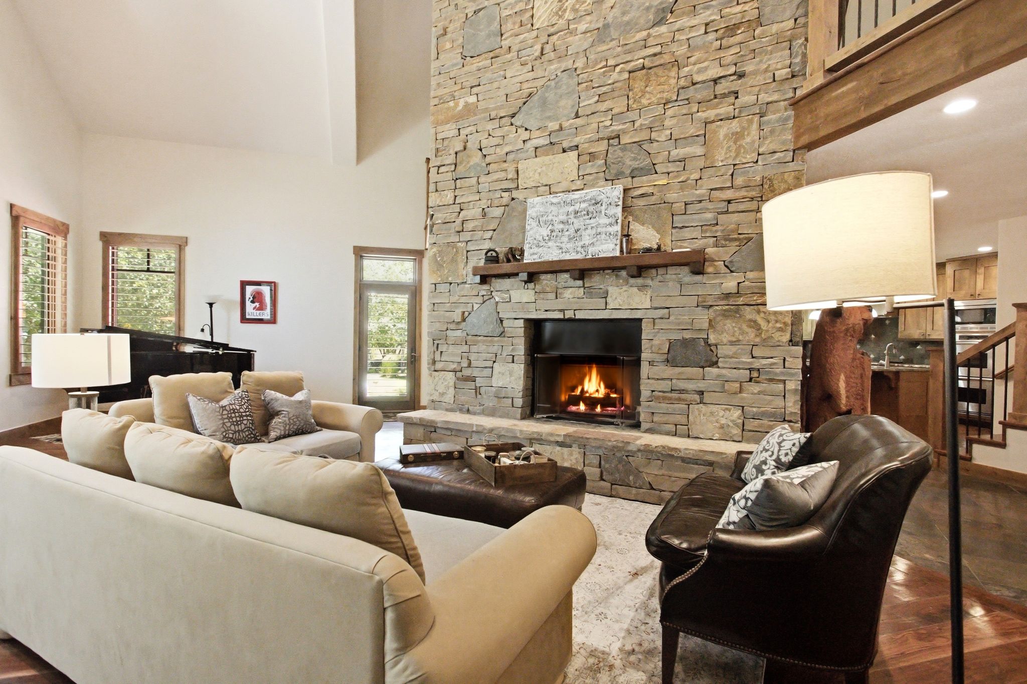 Expansive living area featuring a floor-to-ceiling stone fireplace with a wood mantle, vaulted ceilings, and rich wood-finish flooring
