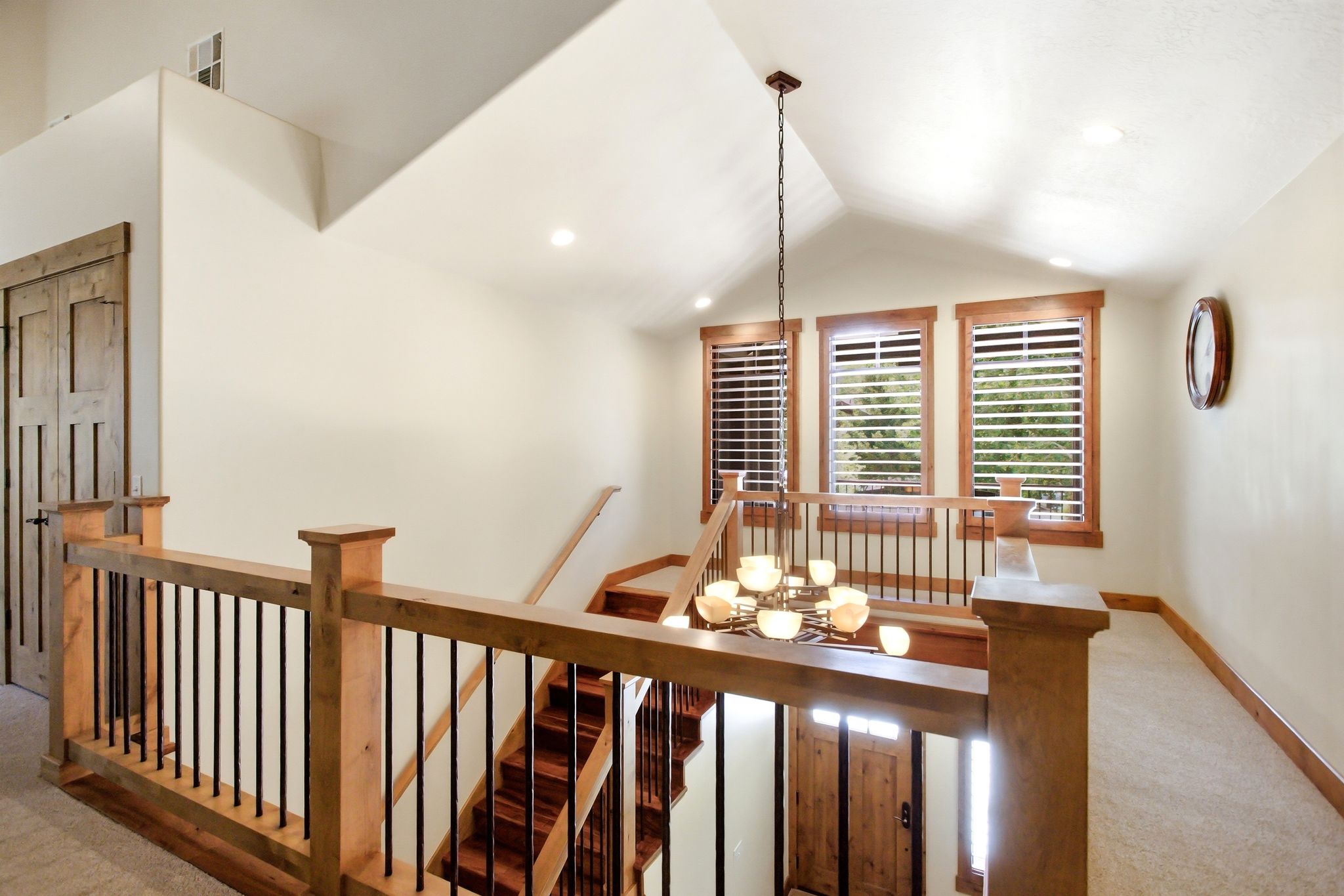 Upper level landing featuring wood-finish railings with black iron balusters, a vaulted ceiling, and recessed lighting