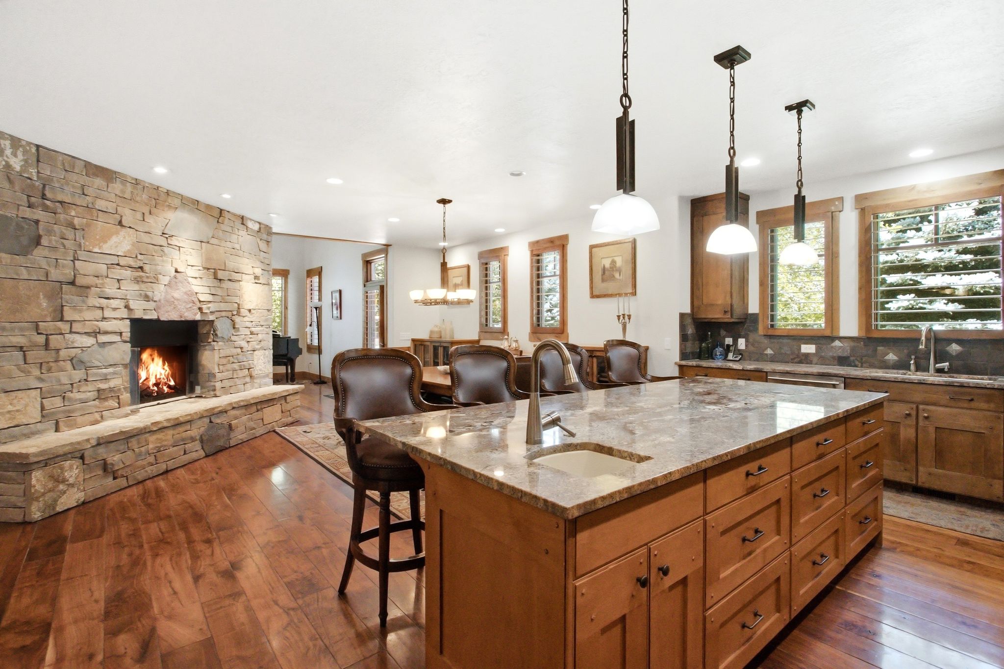 Spacious kitchen featuring a large central island with an undermount sink, stone countertops, and wood-finish flooring