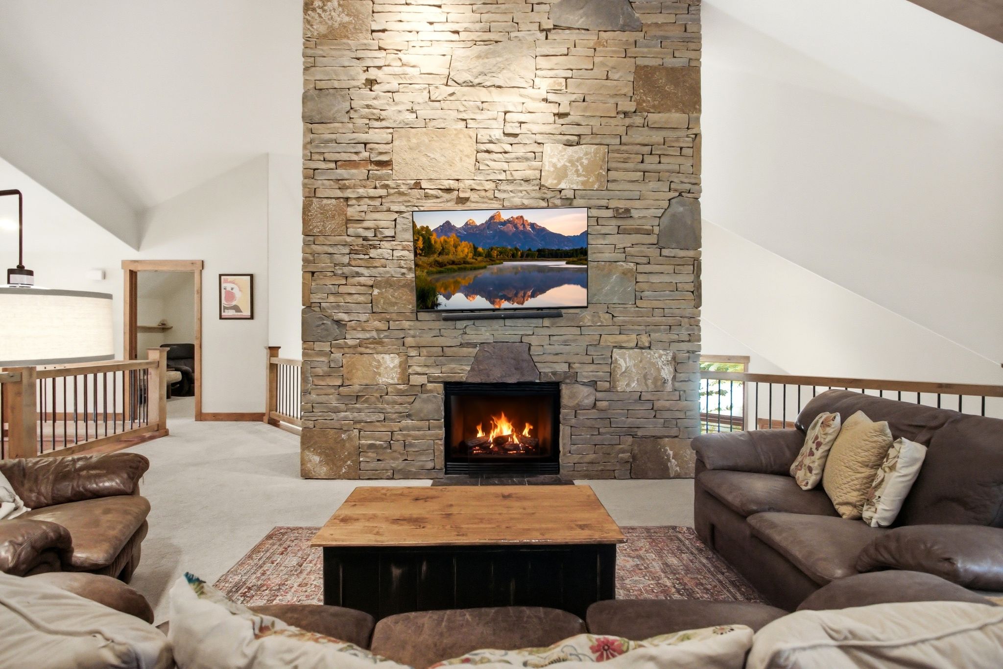 Expansive living area featuring a floor-to-ceiling stone fireplace, vaulted ceilings, and natural wood trim accents