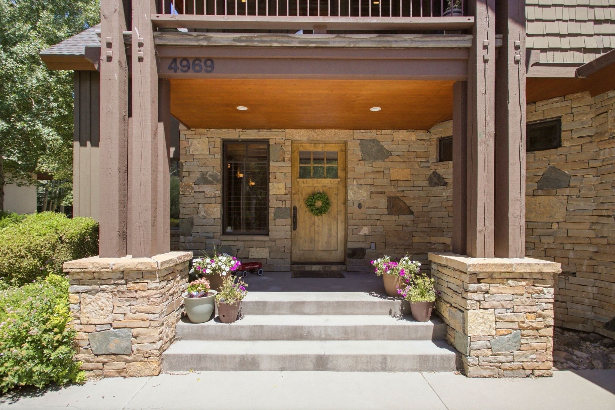 Stone facade entryway with concrete steps, wood-finish pillars, and an overhead wood-finish soffit