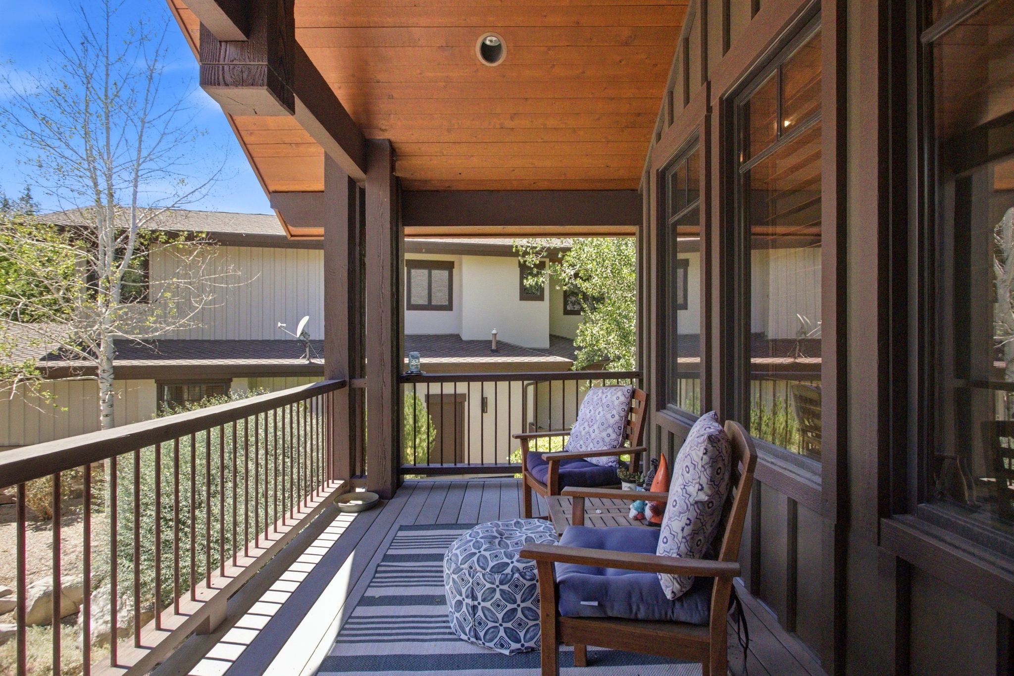 Covered outdoor deck with a wood-finish ceiling, dark wood support beams, and a metal railing