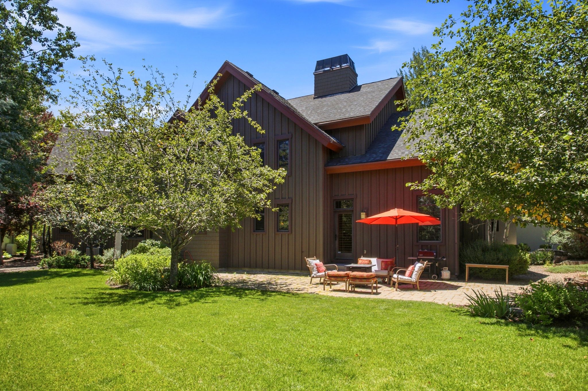 Expansive green lawn with mature trees, a brick paver patio, and dark wood-sided exterior