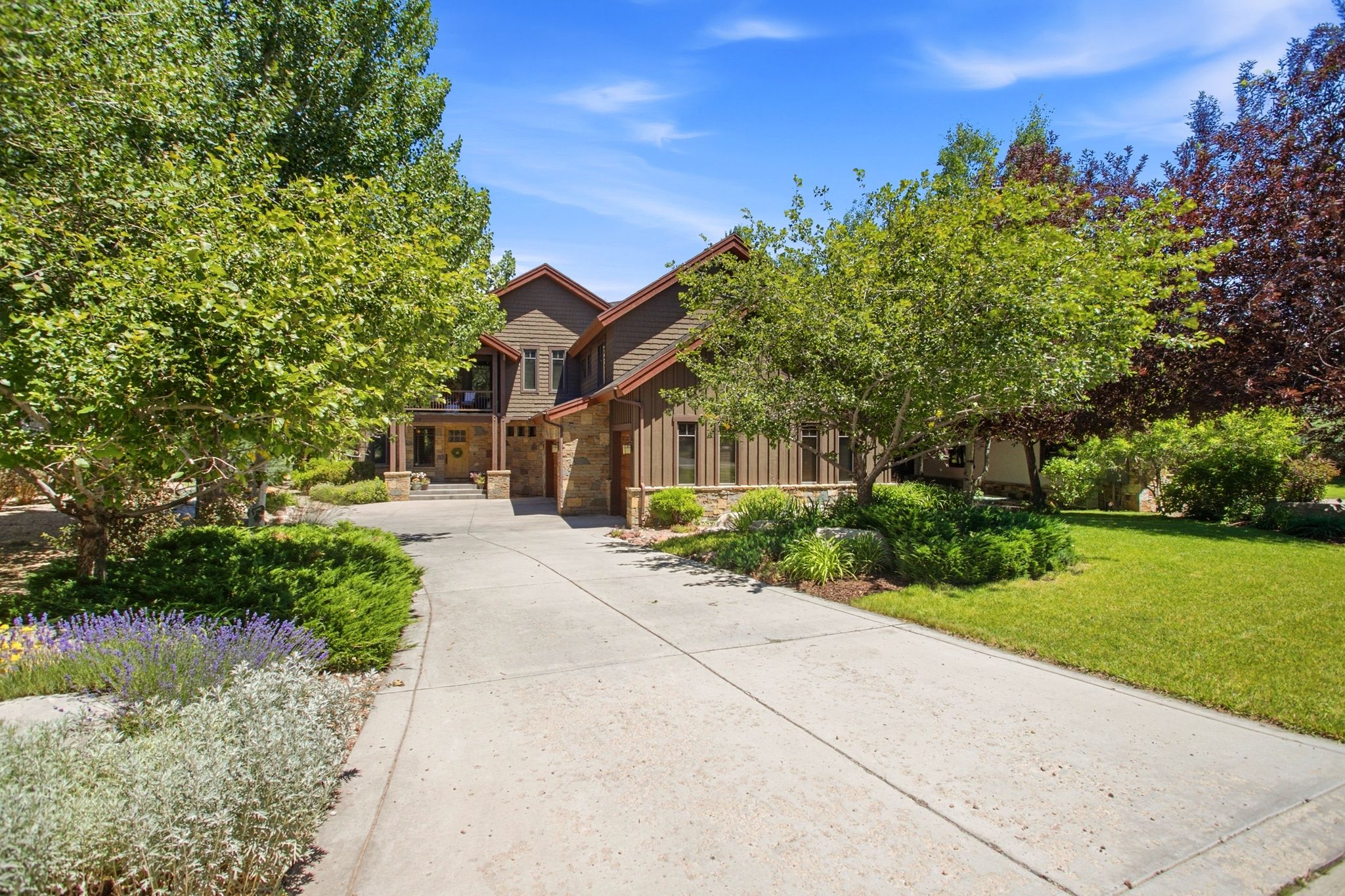 Expansive driveway leading to a multi-level residence featuring stone and wood siding, peaked rooflines, and an integrated garage