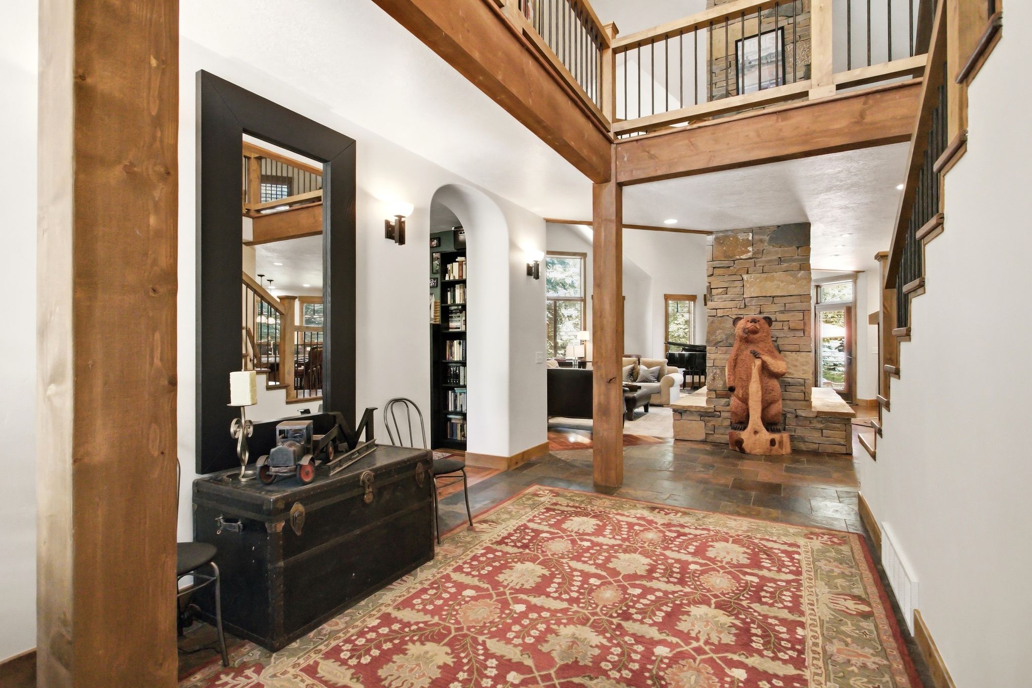 Two-story entry featuring exposed wood beams, slate tile flooring, a stone fireplace, an arched entryway, and a built-in bookshelf