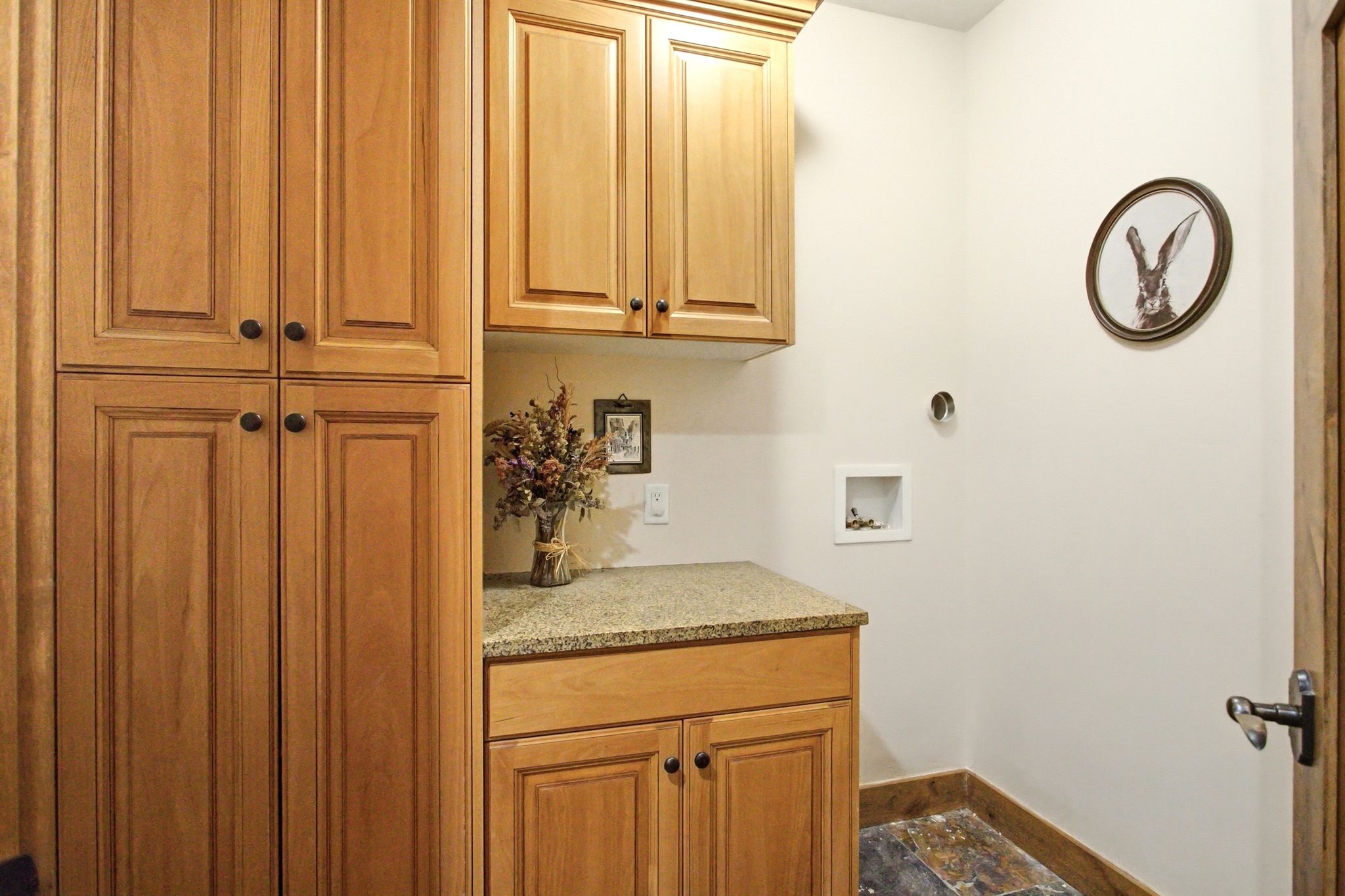 Laundry area featuring wood cabinetry with black hardware, a light-toned countertop, and slate tile flooring